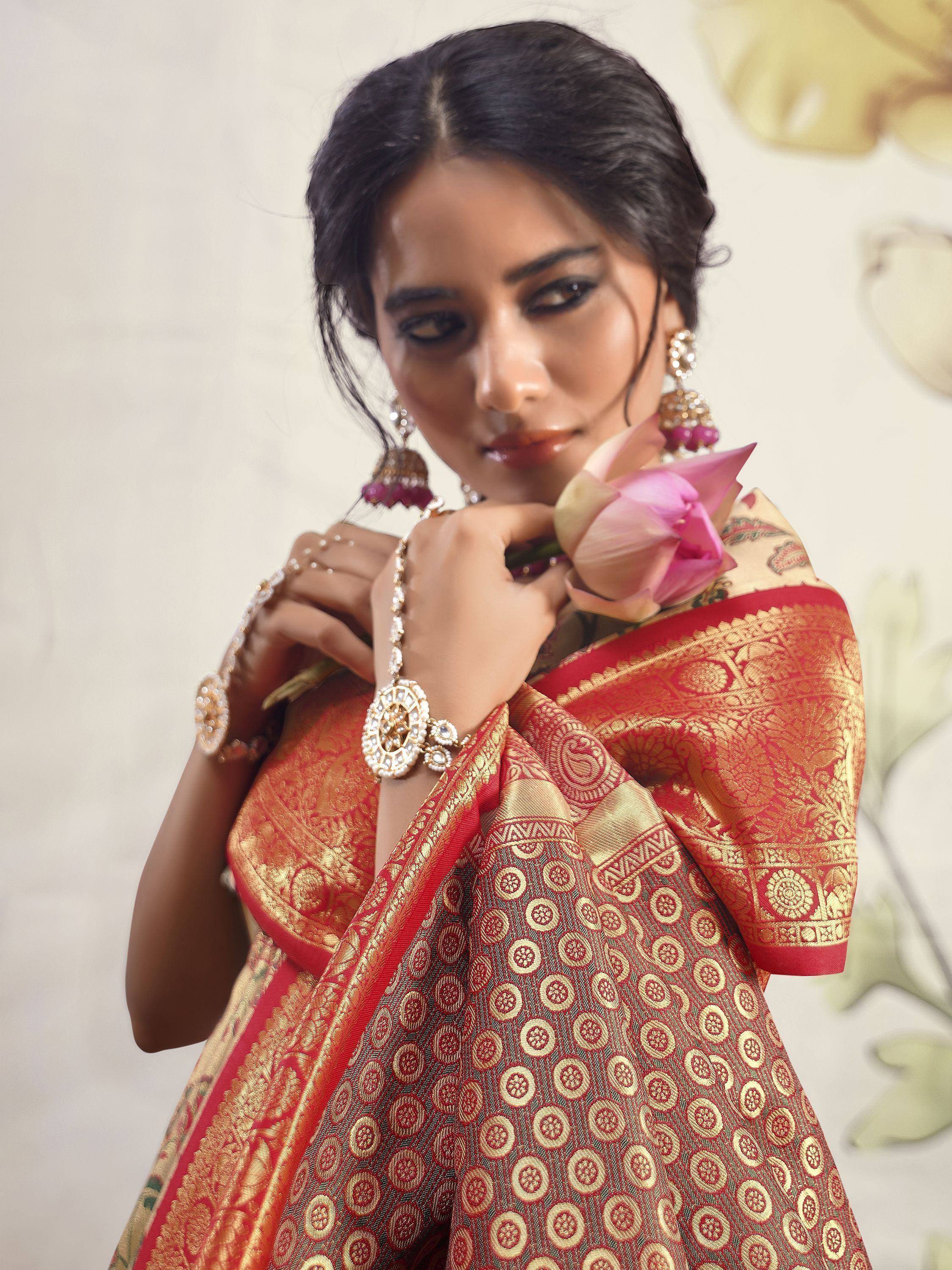 Woman in red and gold designer saree with intricate patterns, holding pink lotus, traditional Indian ethnic wear