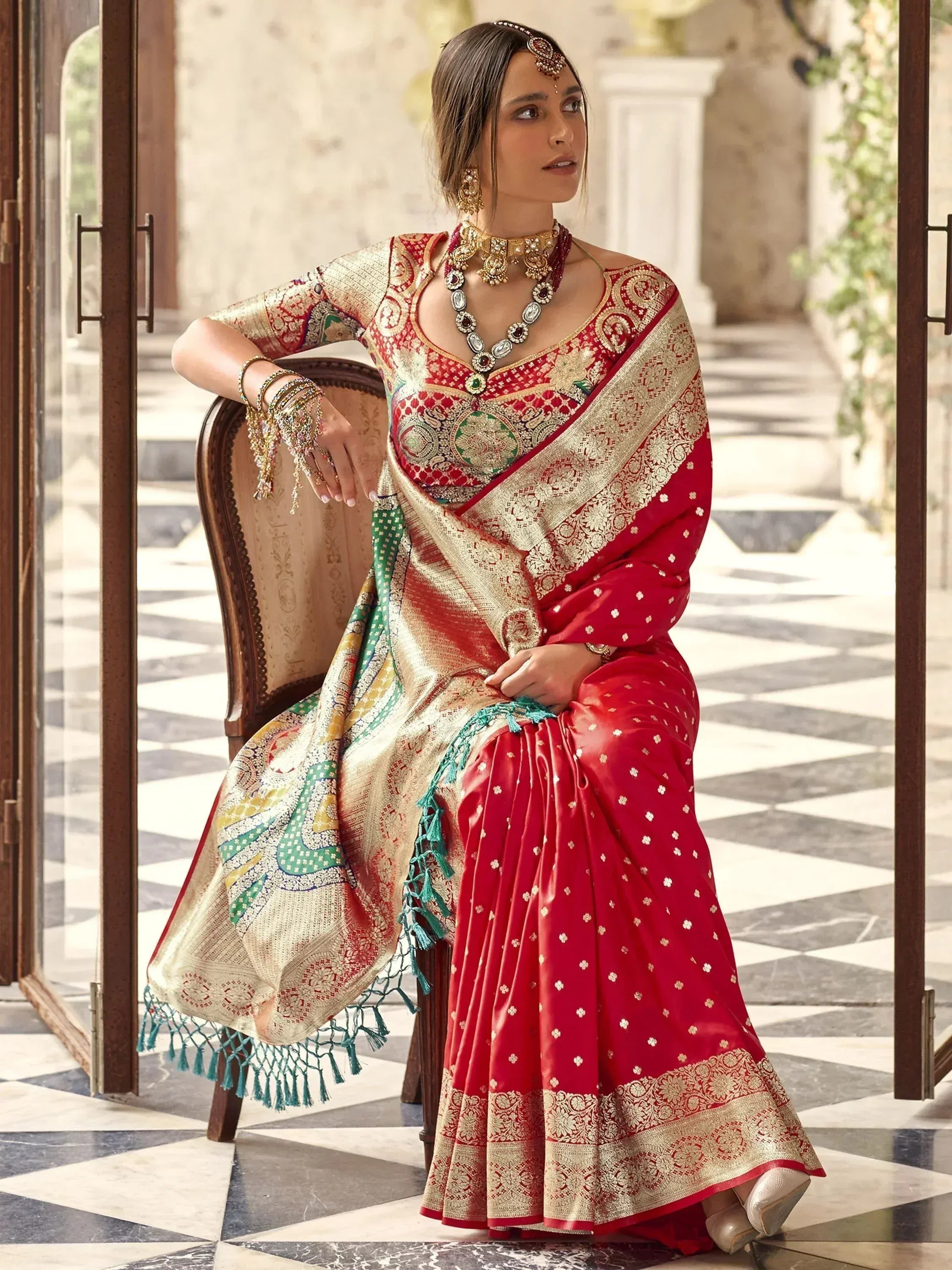 Red and gold designer saree with intricate embroidery and tassels, paired with traditional jewelry