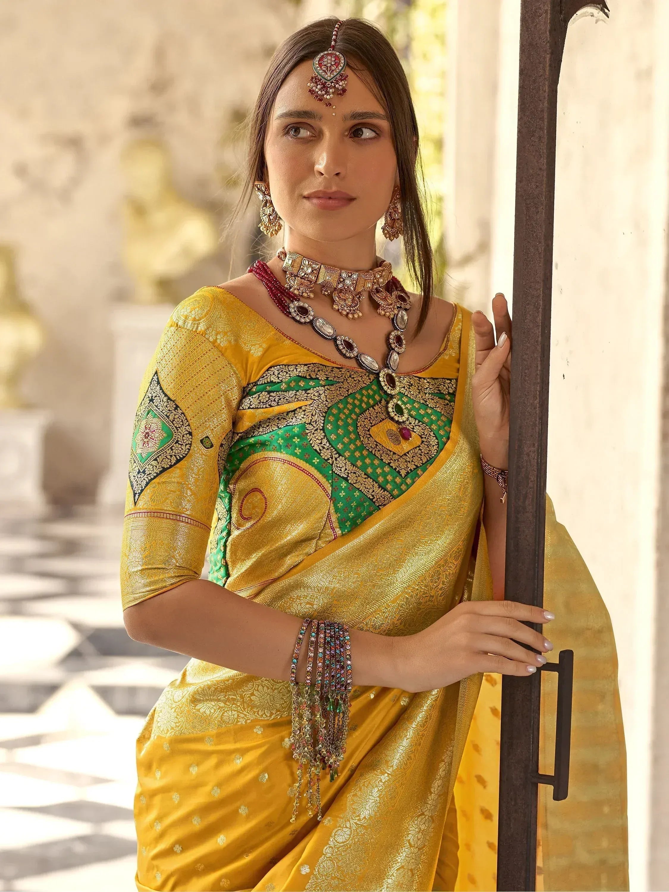 Woman in yellow and green designer saree with intricate embroidery and traditional Indian jewelry