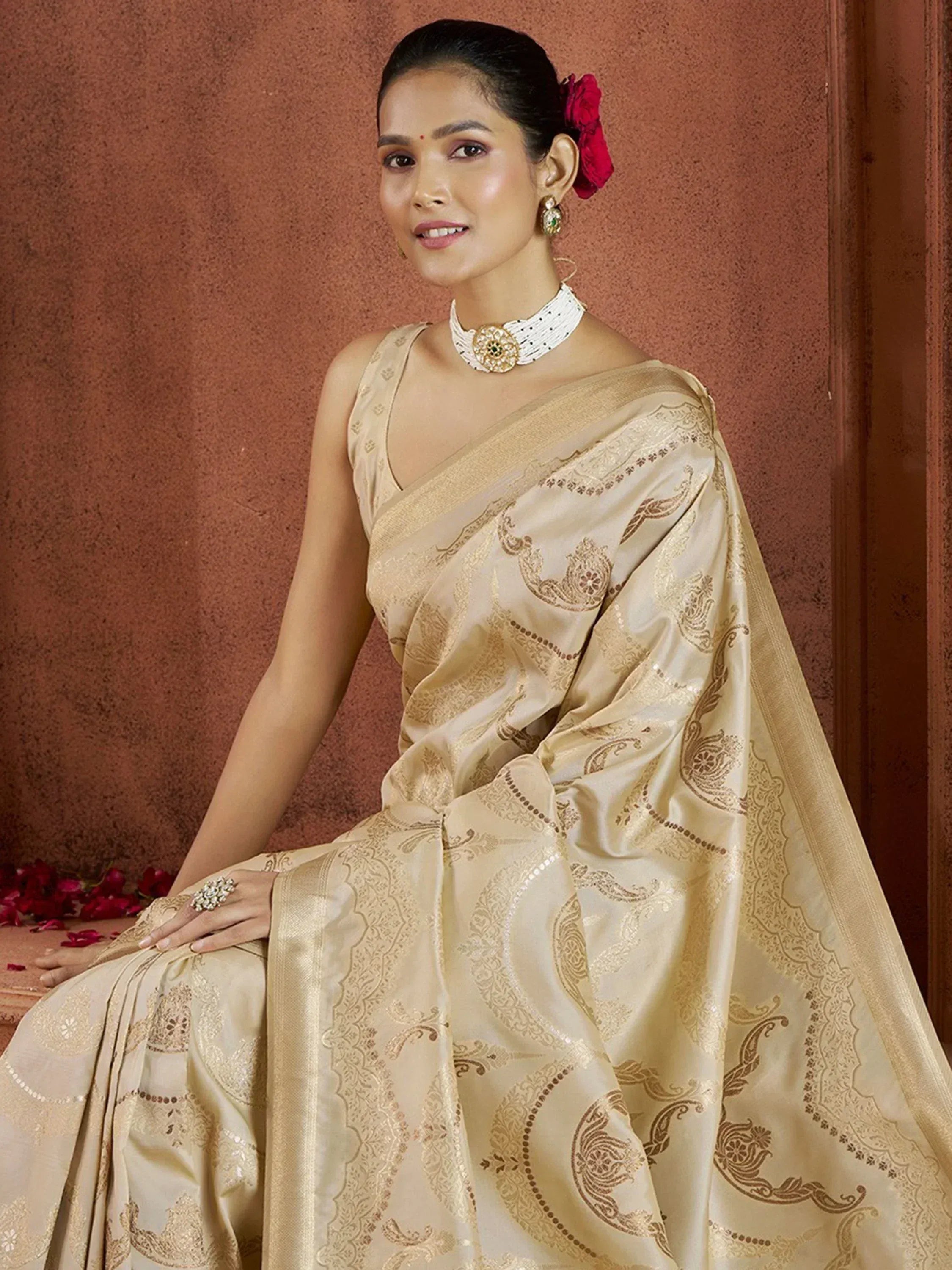 Elegant beige saree with gold paisley embroidery, styled with choker and red floral hair accessory
