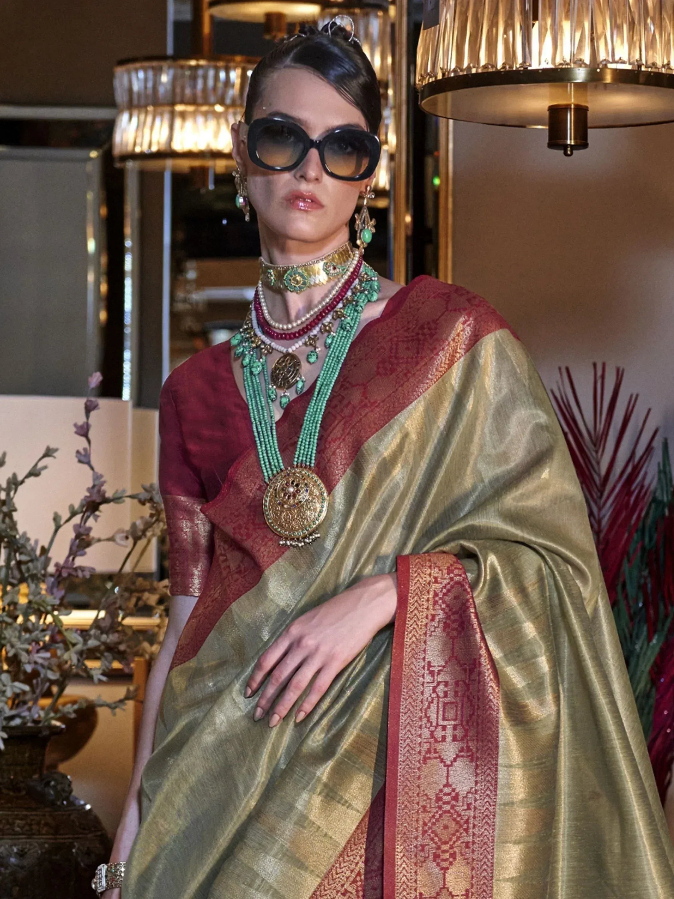 Elegant woman in gold and red ethnic saree with traditional jewelry and sunglasses, styled for festive occasions.