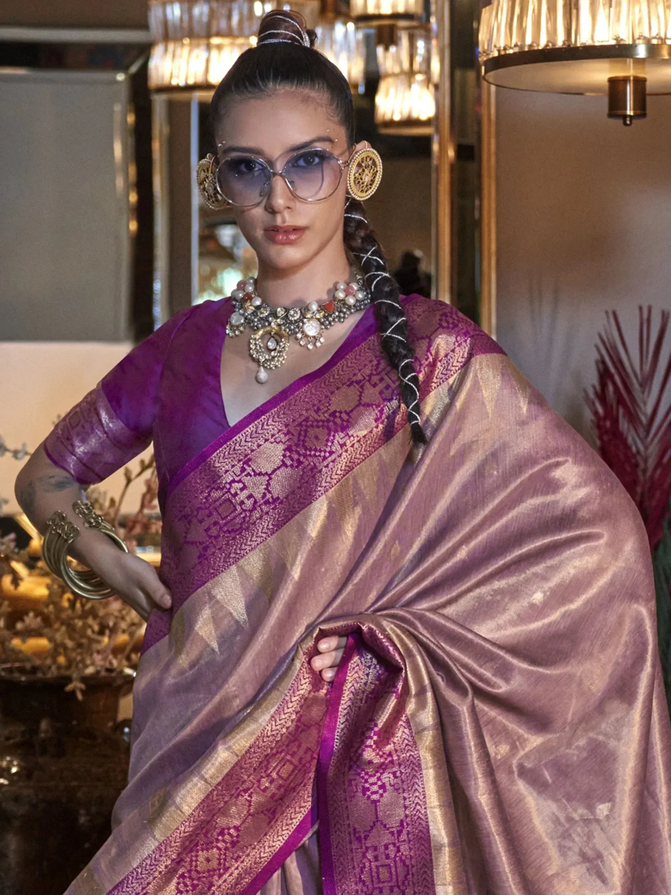 Purple and gold designer saree with intricate woven patterns, paired with statement jewelry and modern sunglasses