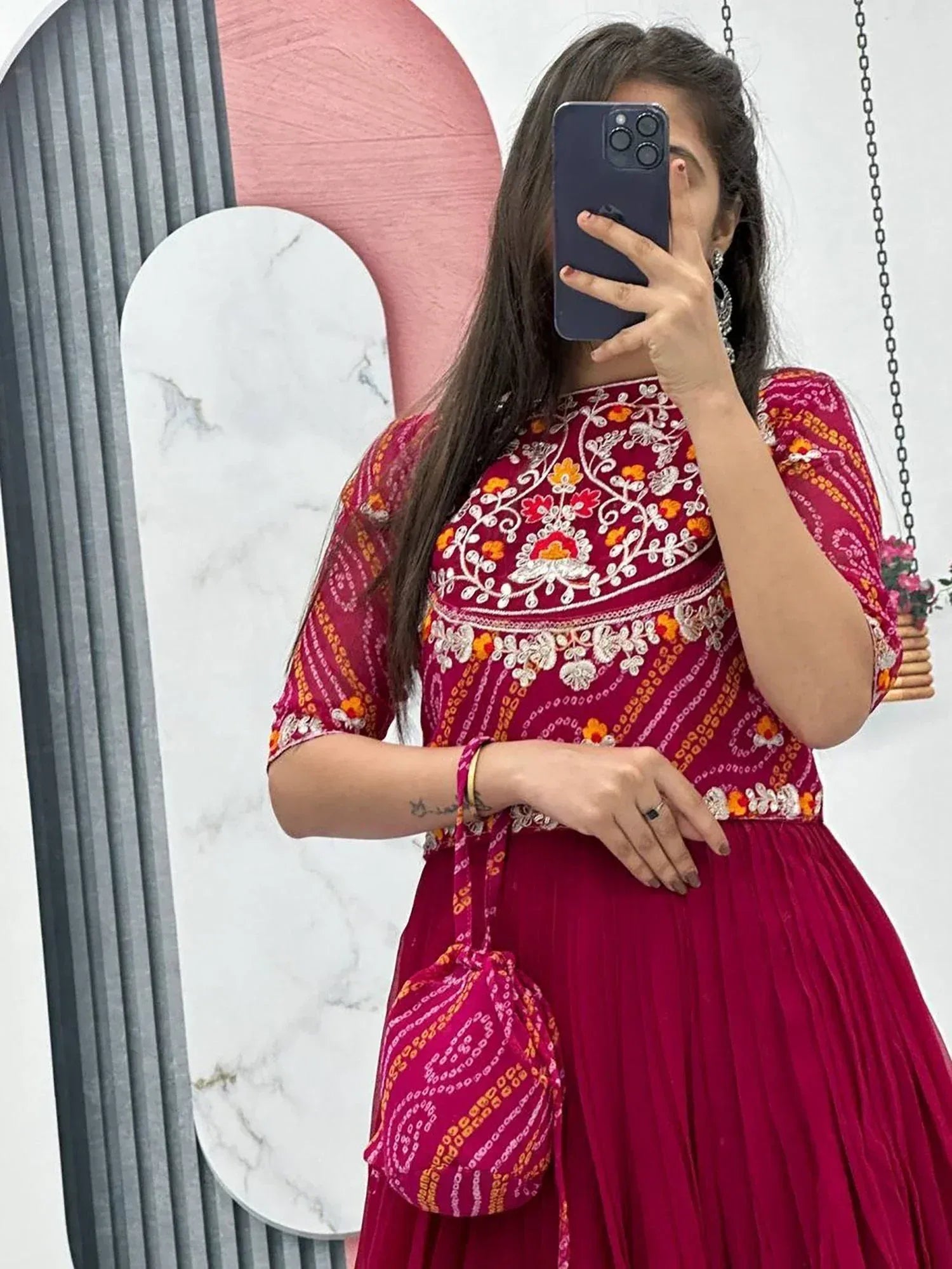 Woman in maroon embroidered ethnic gown with floral patterns, matching potli bag, taking mirror selfie