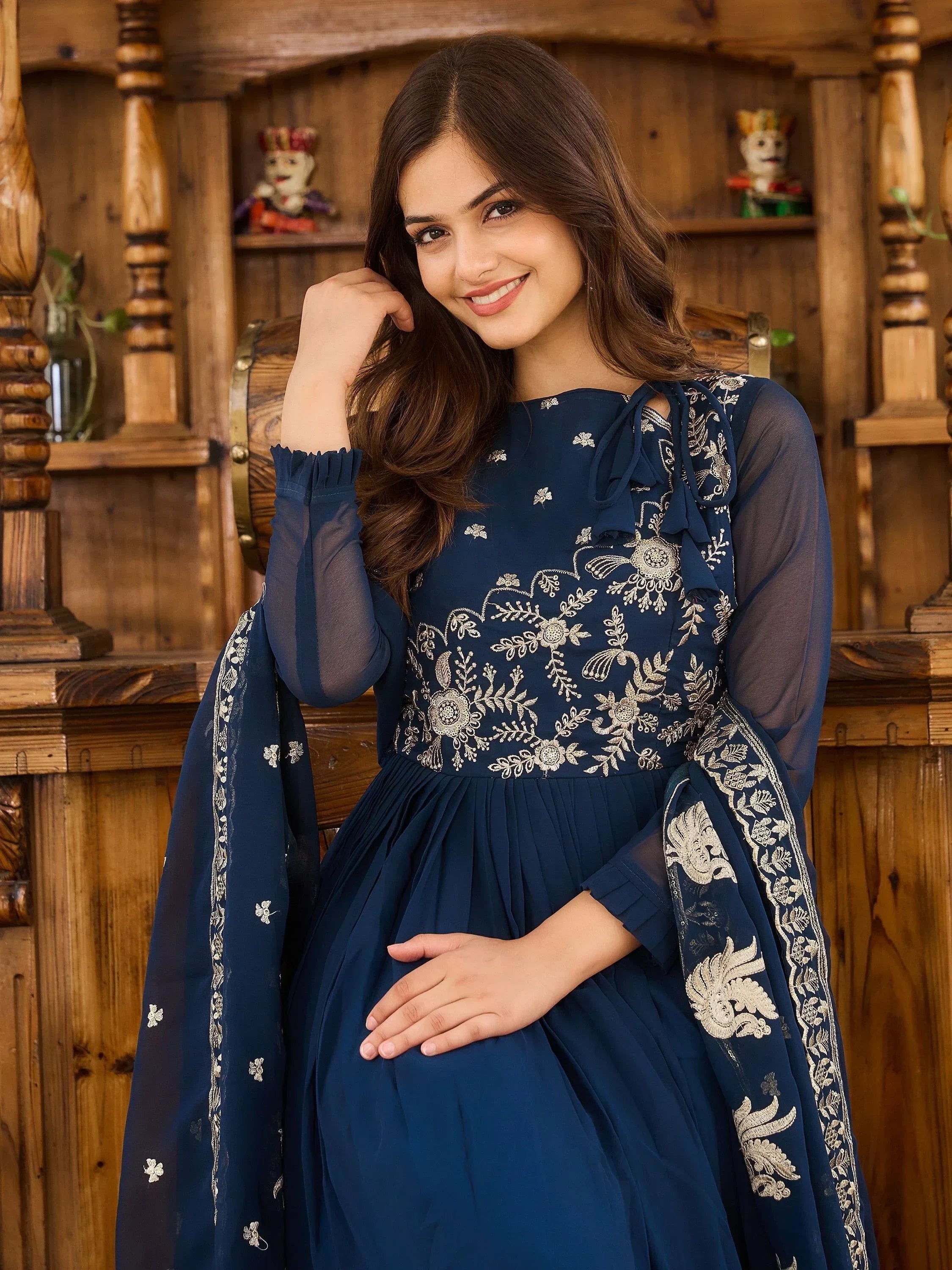 Woman in navy blue embroidered ethnic gown with sheer sleeves and dupatta, wooden background