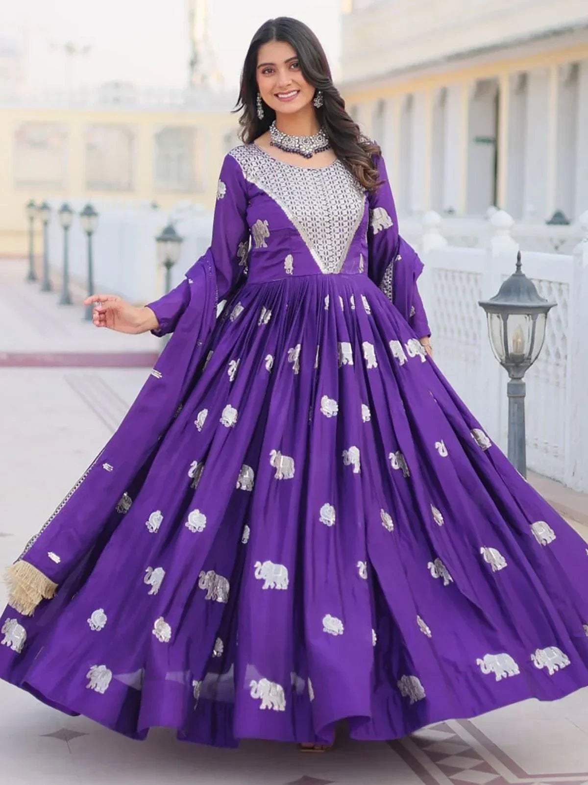 Woman in purple embroidered Anarkali gown with silver elephant motifs, standing outdoors