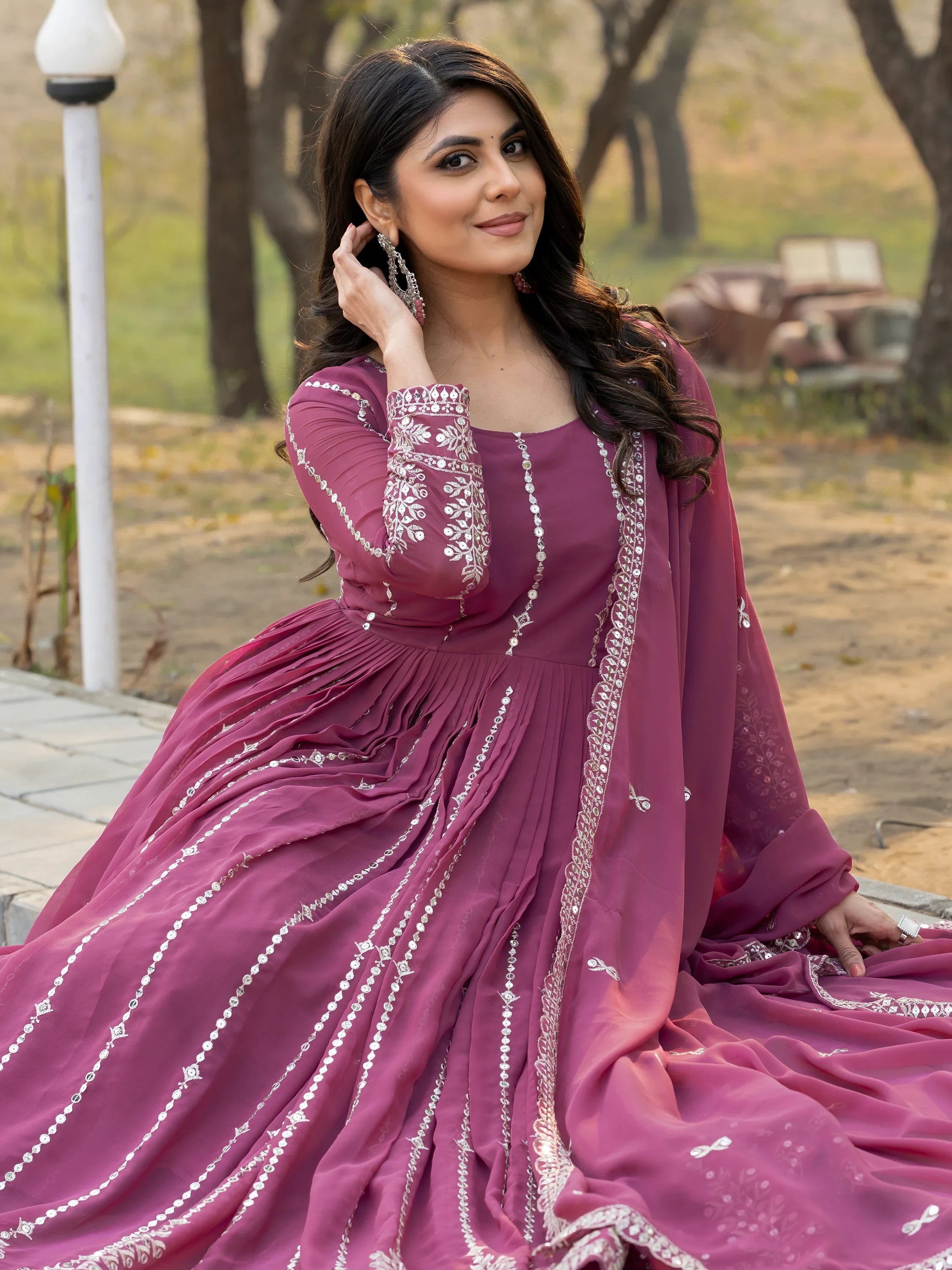 Woman in pink embroidered Indian ethnic gown sitting outdoors, wearing statement earrings