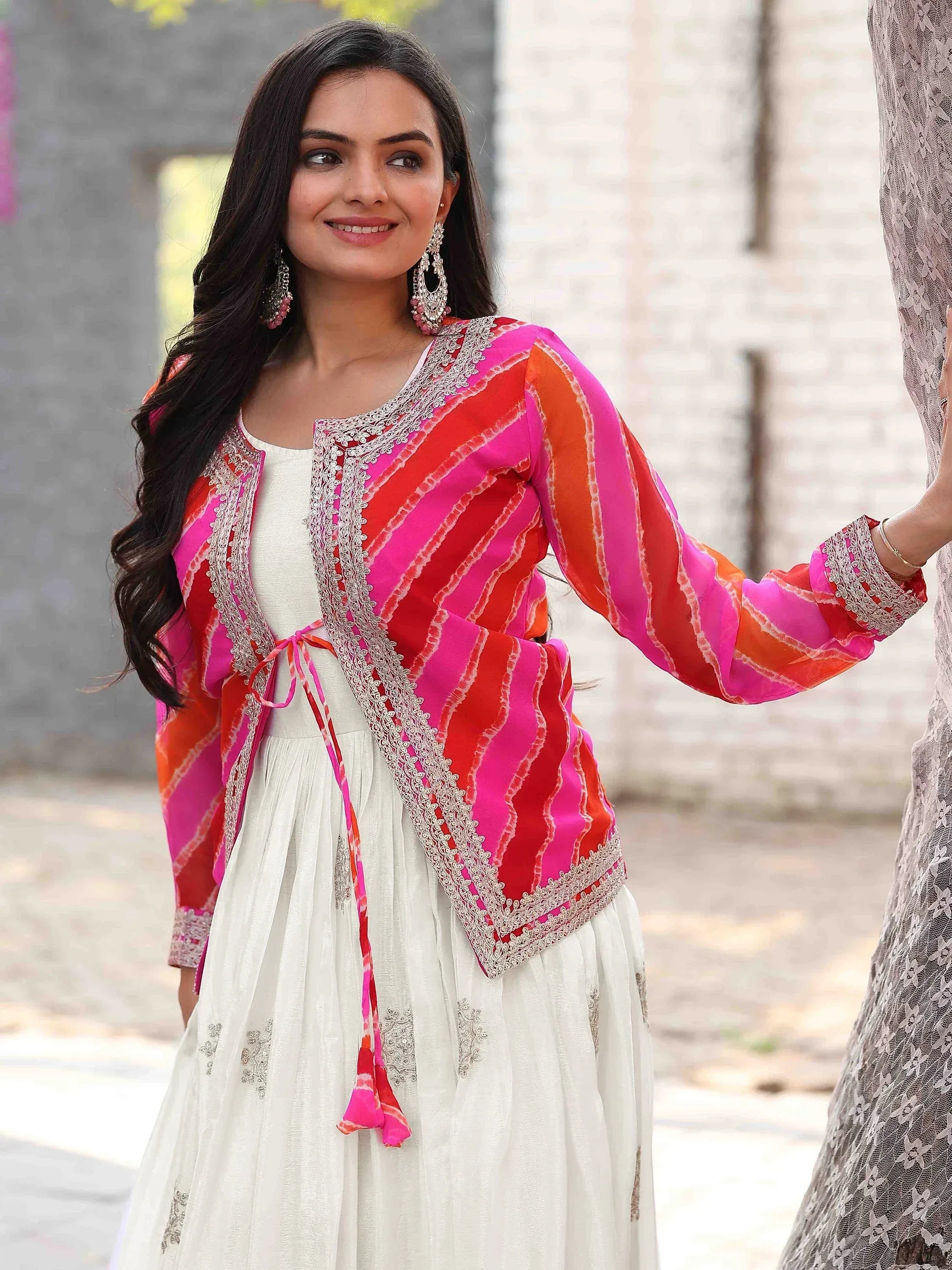 Woman in vibrant pink and orange striped ethnic jacket with white embroidered dress