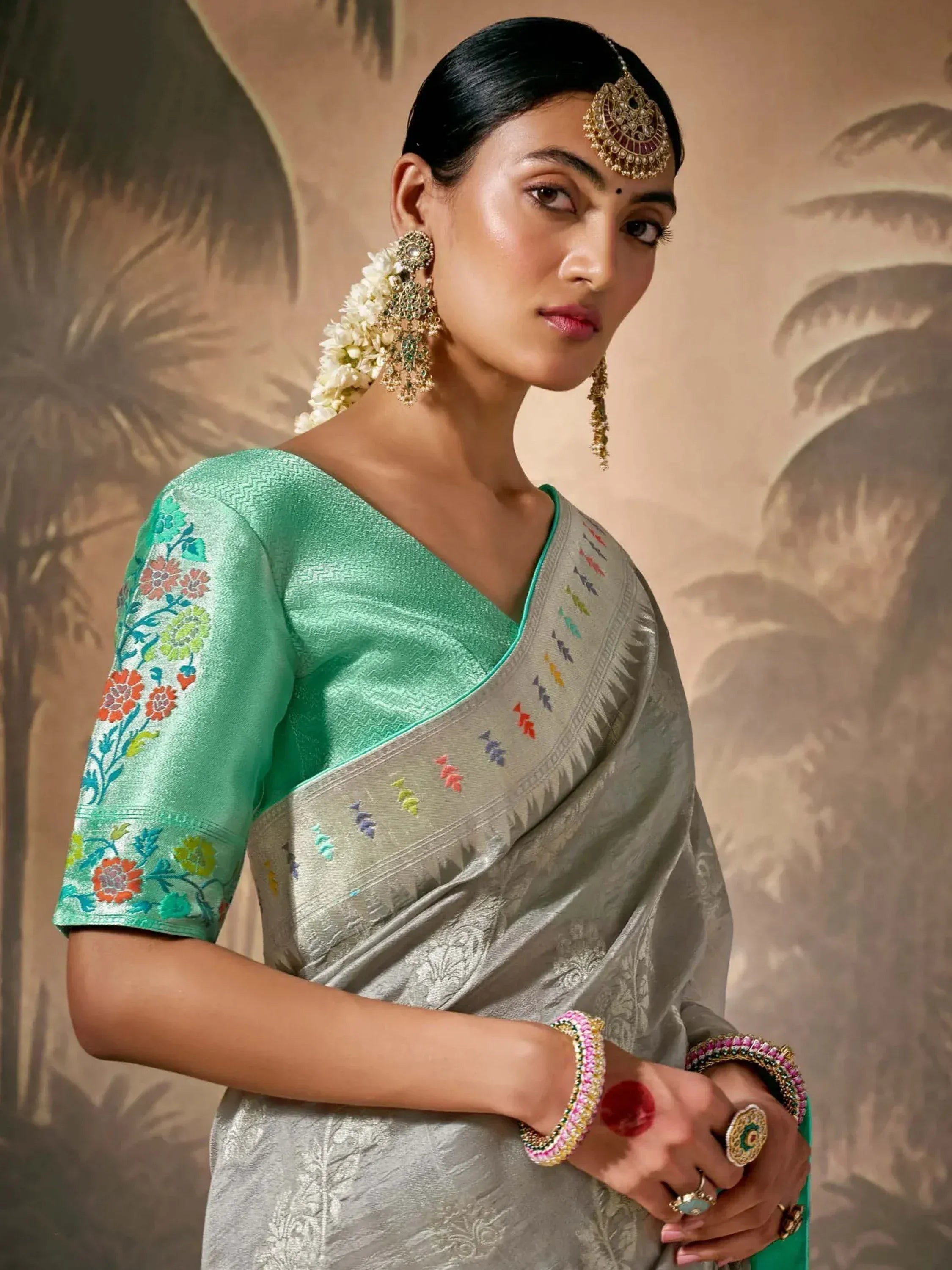 Woman in elegant silver saree with green embroidered blouse, traditional Indian jewelry, floral hair accessory