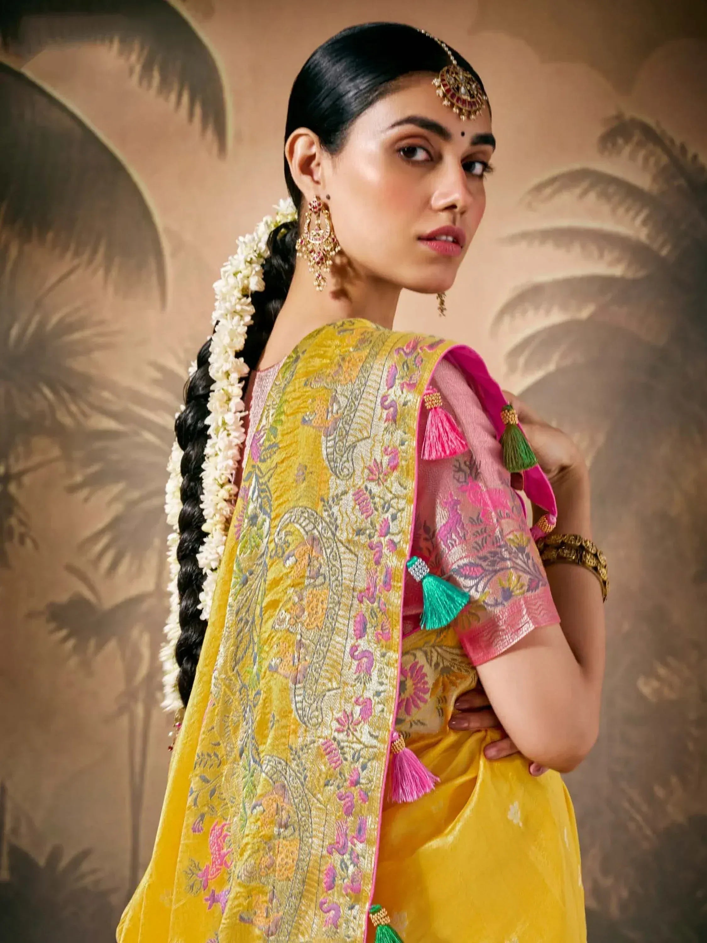 Yellow embroidered Indian ethnic saree with pink tassels, floral hair garland, and traditional jewelry