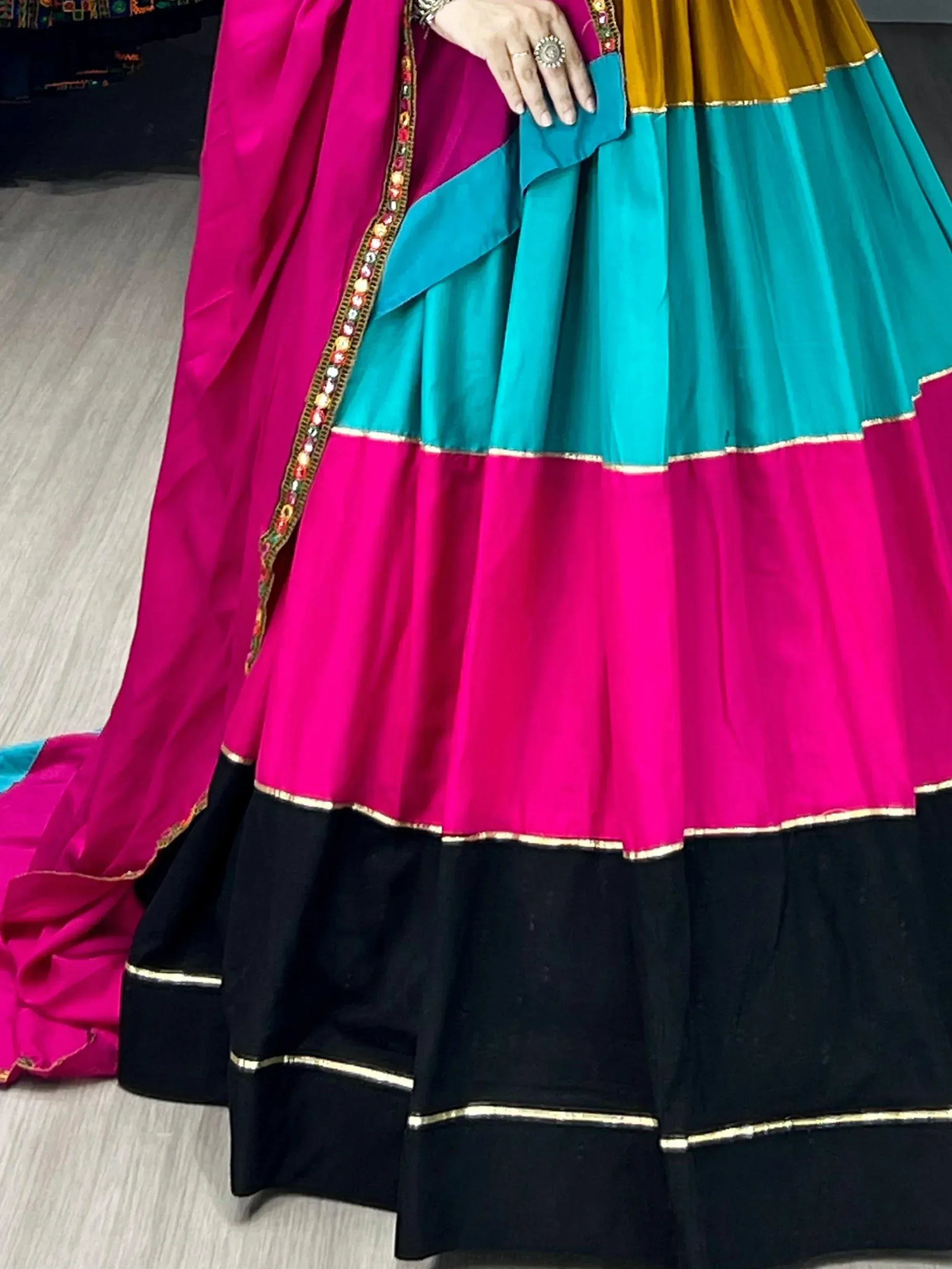 Vibrant multi-color lehenga choli with pink, teal, mustard, and black tiers, gold trim, and embellished dupatta.
