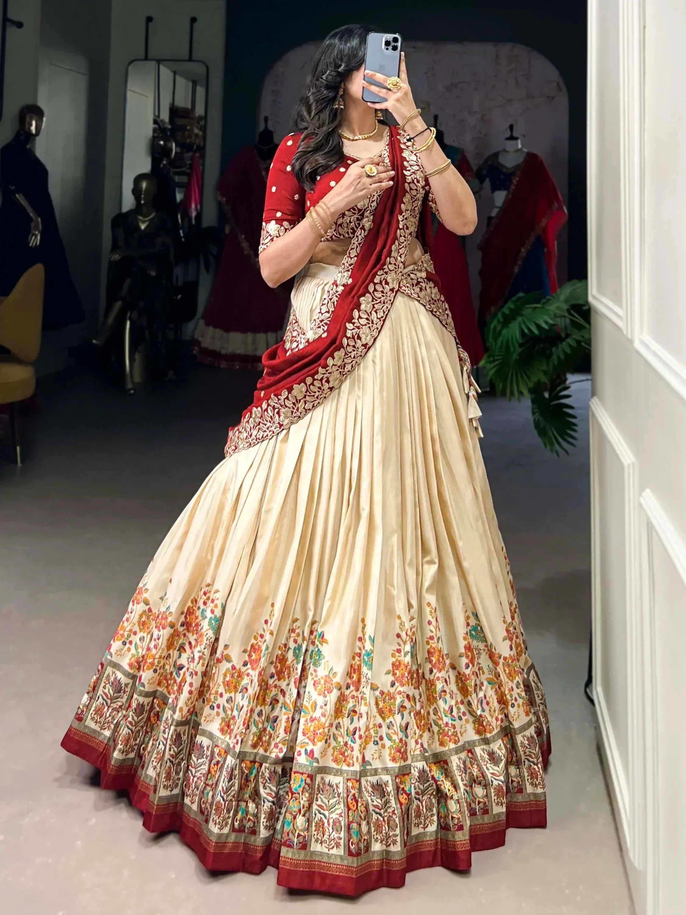 Woman in red and cream embroidered lehenga choli taking mirror selfie, floral border, ethnic Indian wear