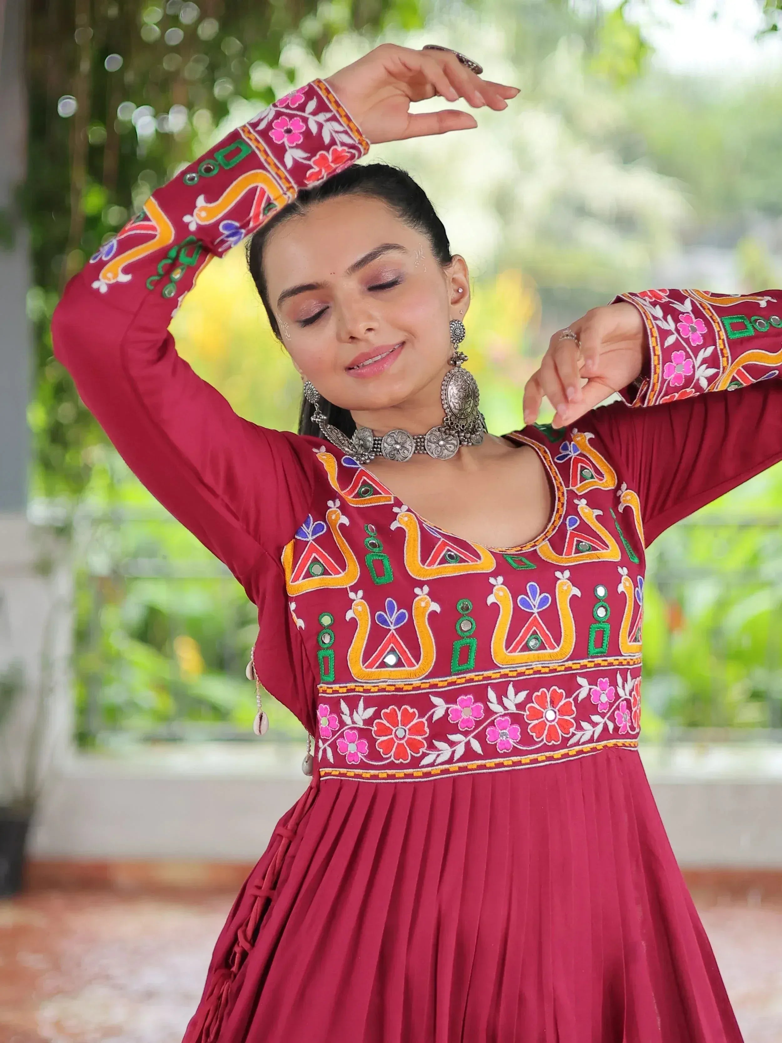 Woman in maroon ethnic gown with colorful embroidery and mirror work, styled with traditional jewelry