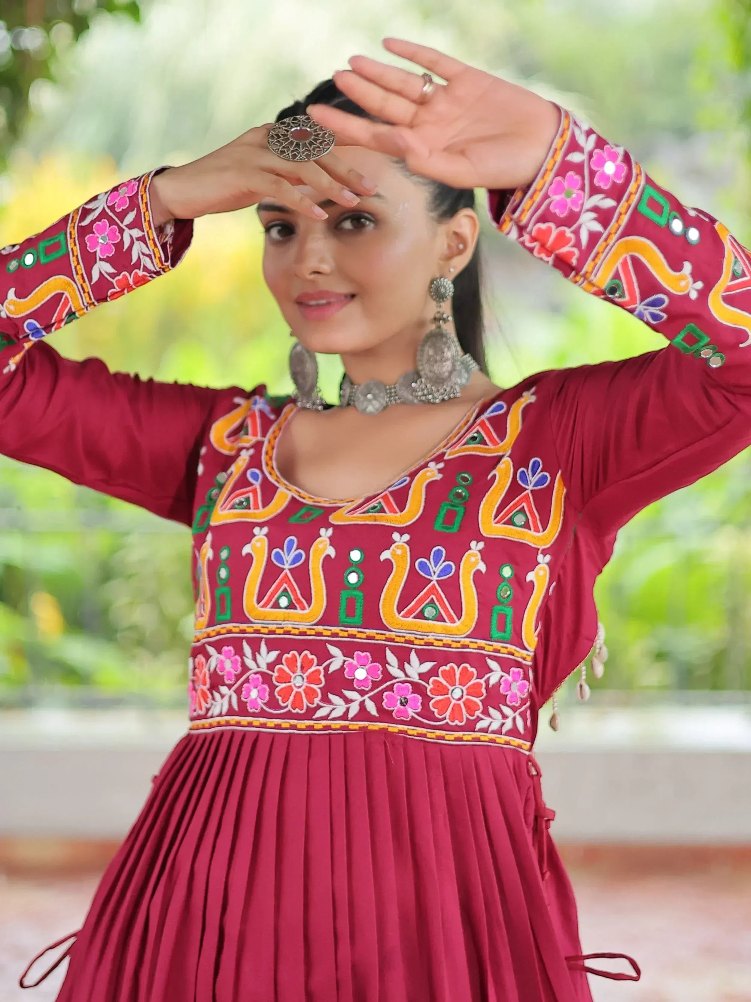 Maroon ethnic gown with colorful mirror embroidery and floral patterns, paired with traditional jewelry