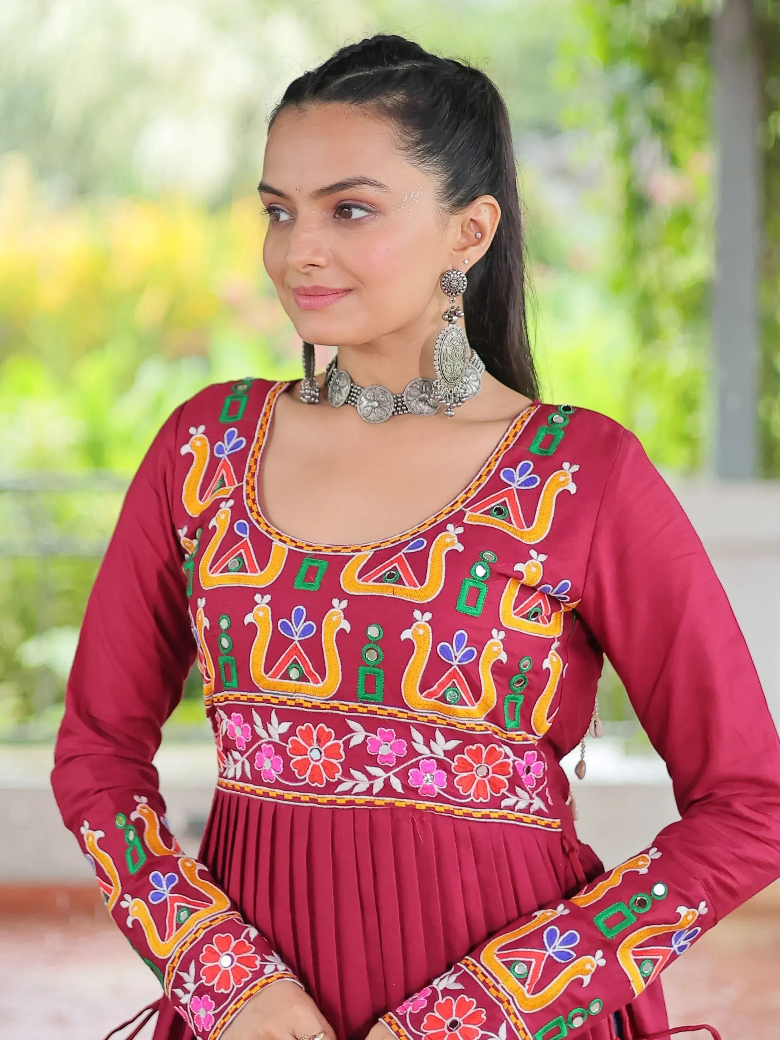 Maroon ethnic gown with colorful peacock embroidery and mirror work, paired with silver jewelry