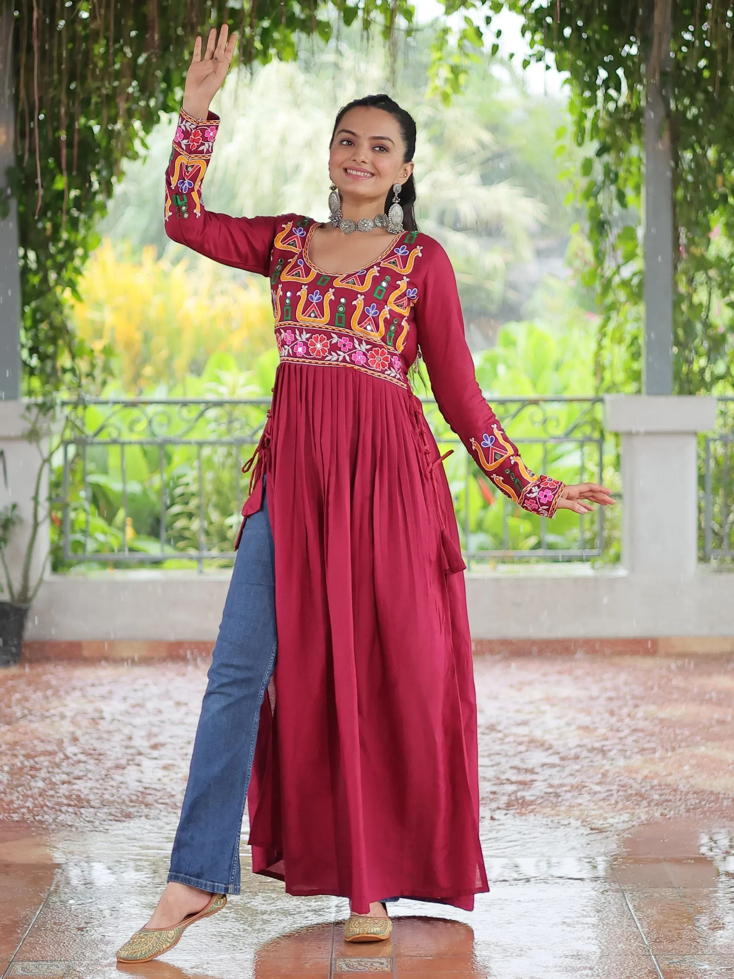 Woman in maroon embroidered ethnic gown with jeans, smiling outdoors in rain