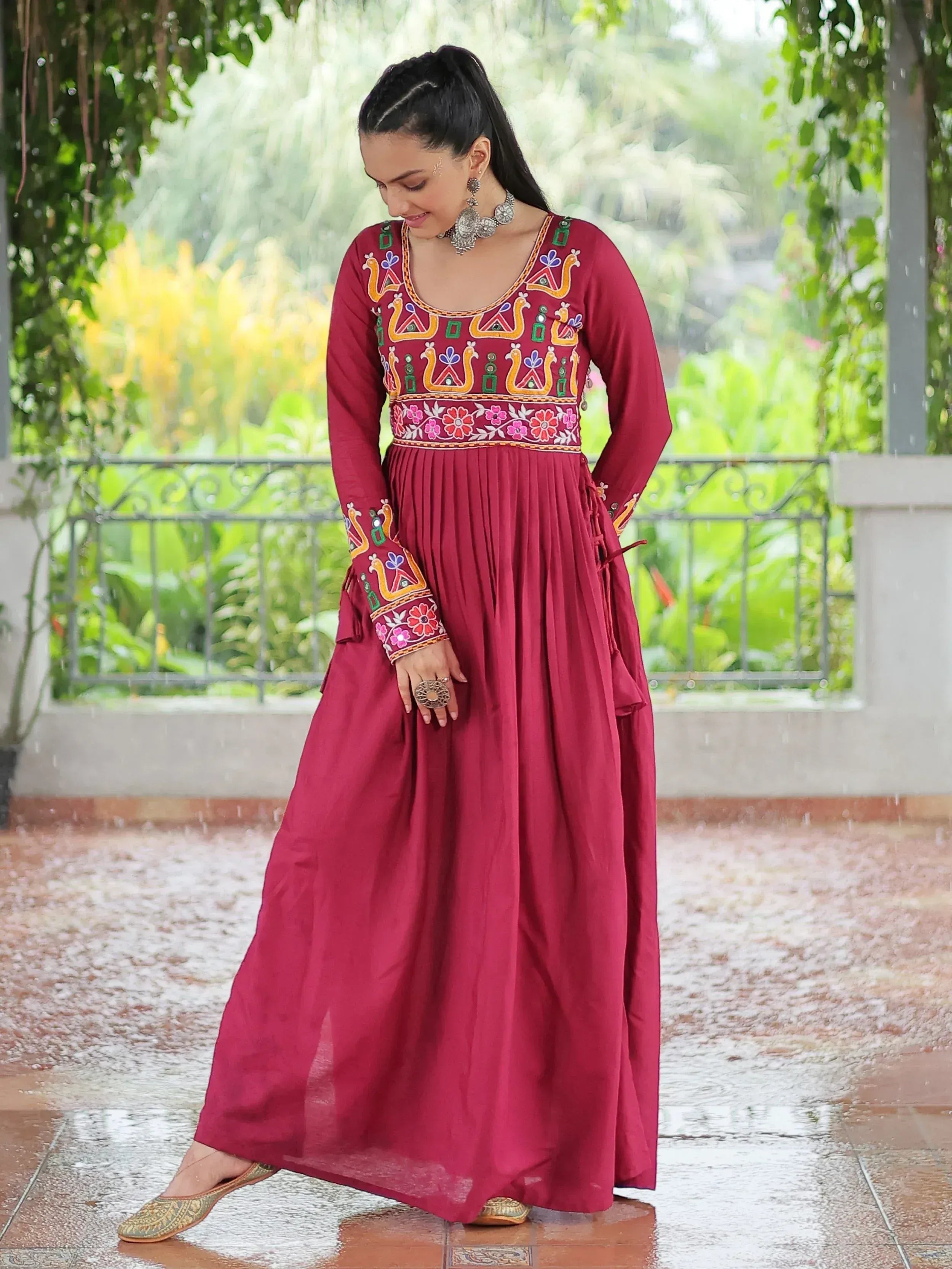 Maroon ethnic gown with colorful embroidery, floral patterns, and traditional jewelry, perfect for Indian occasions.