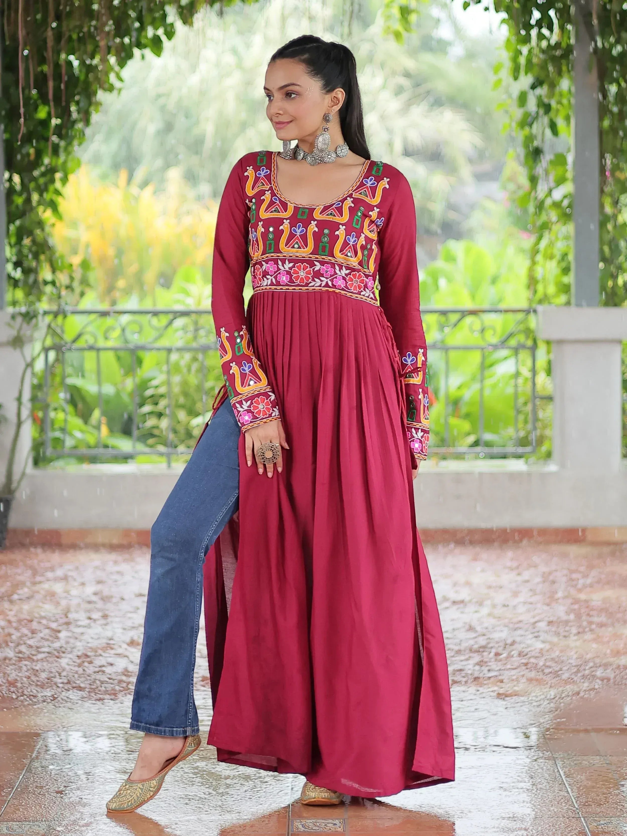 Maroon embroidered ethnic gown with peacock motifs, paired with jeans and juttis for fusion wear