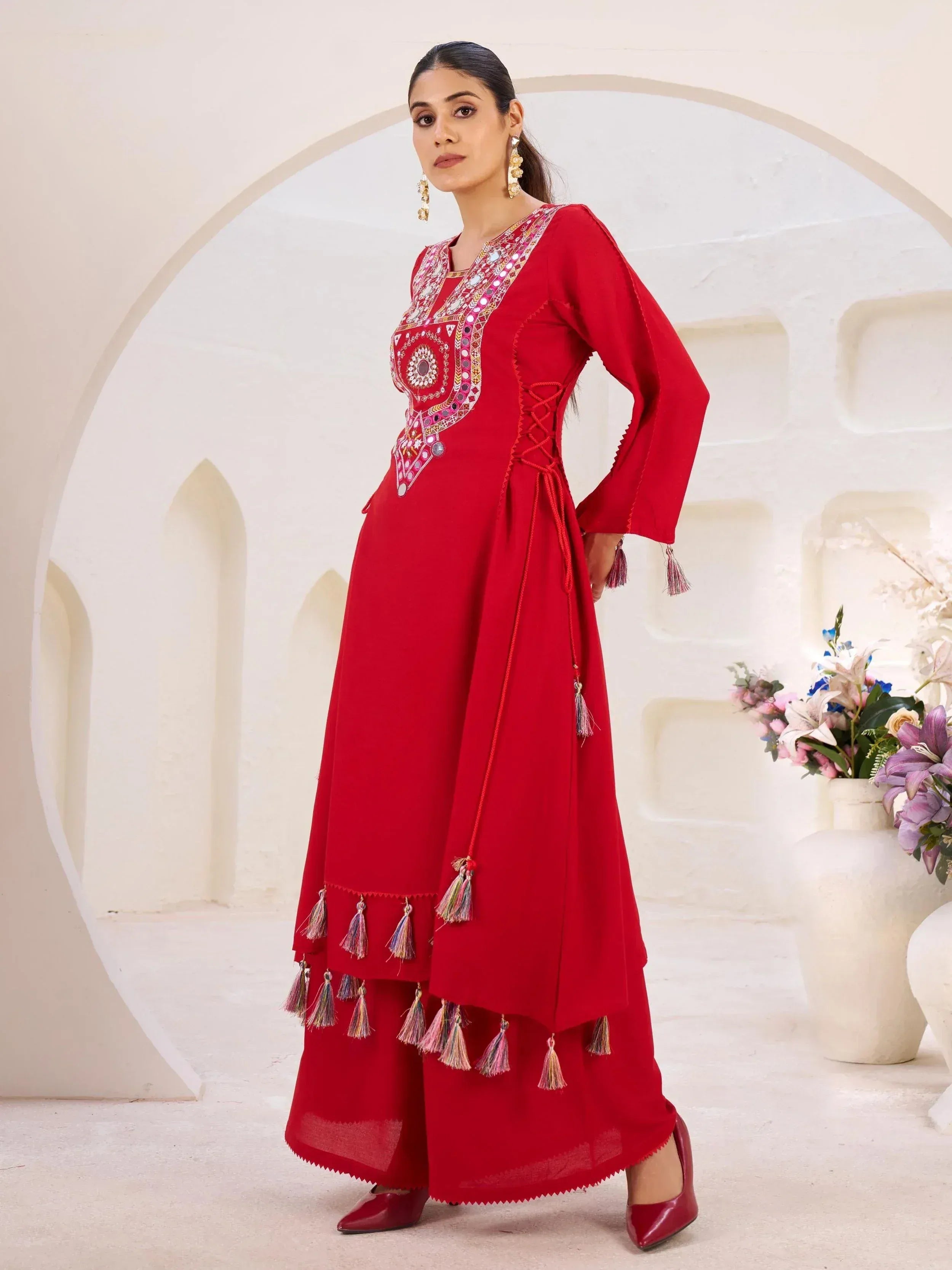 Red ethnic gown with mirror work and tassels, paired with palazzo pants for festive occasions