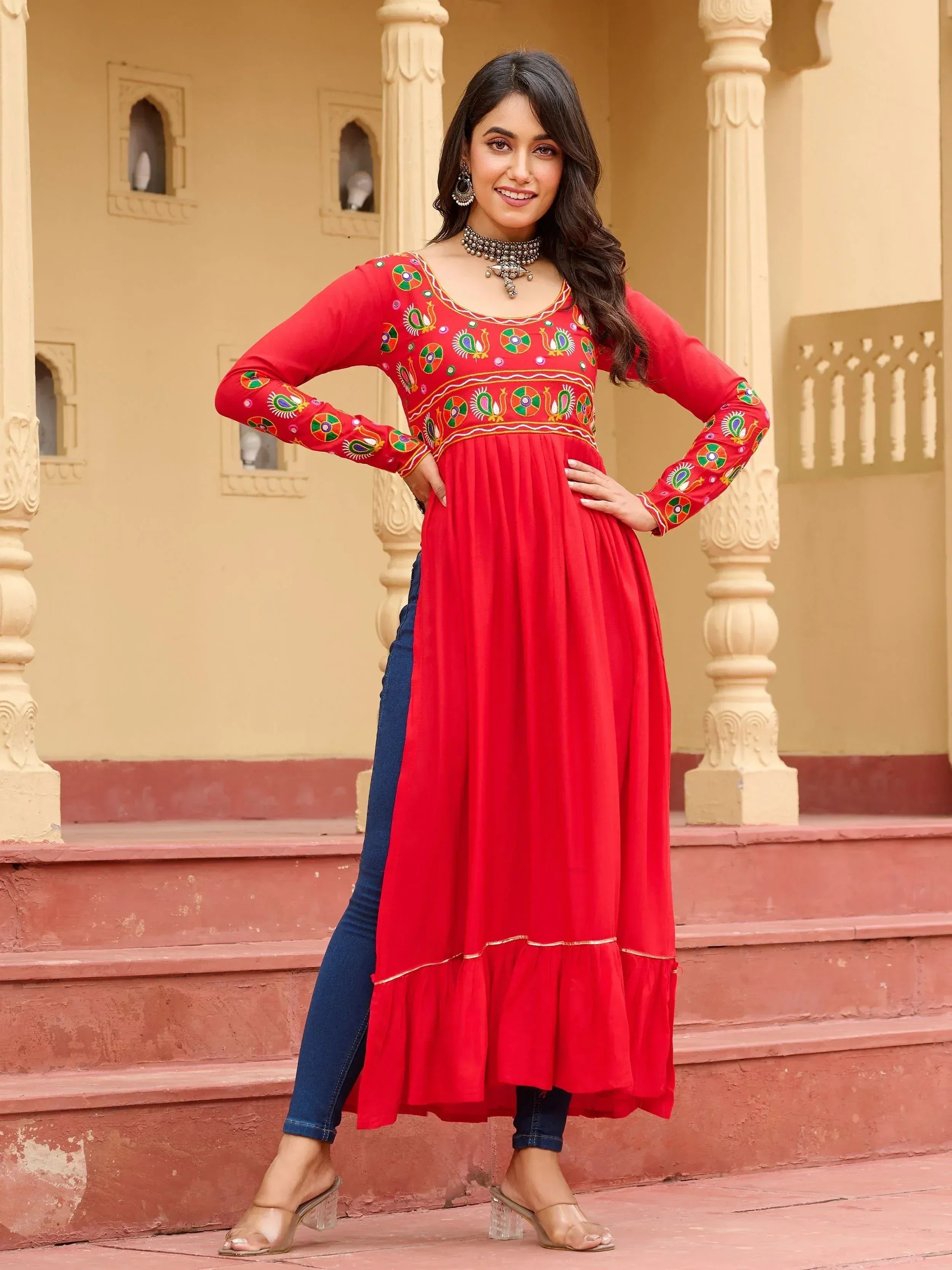 Red embroidered ethnic gown with peacock motifs paired with jeans, perfect for festive occasions.