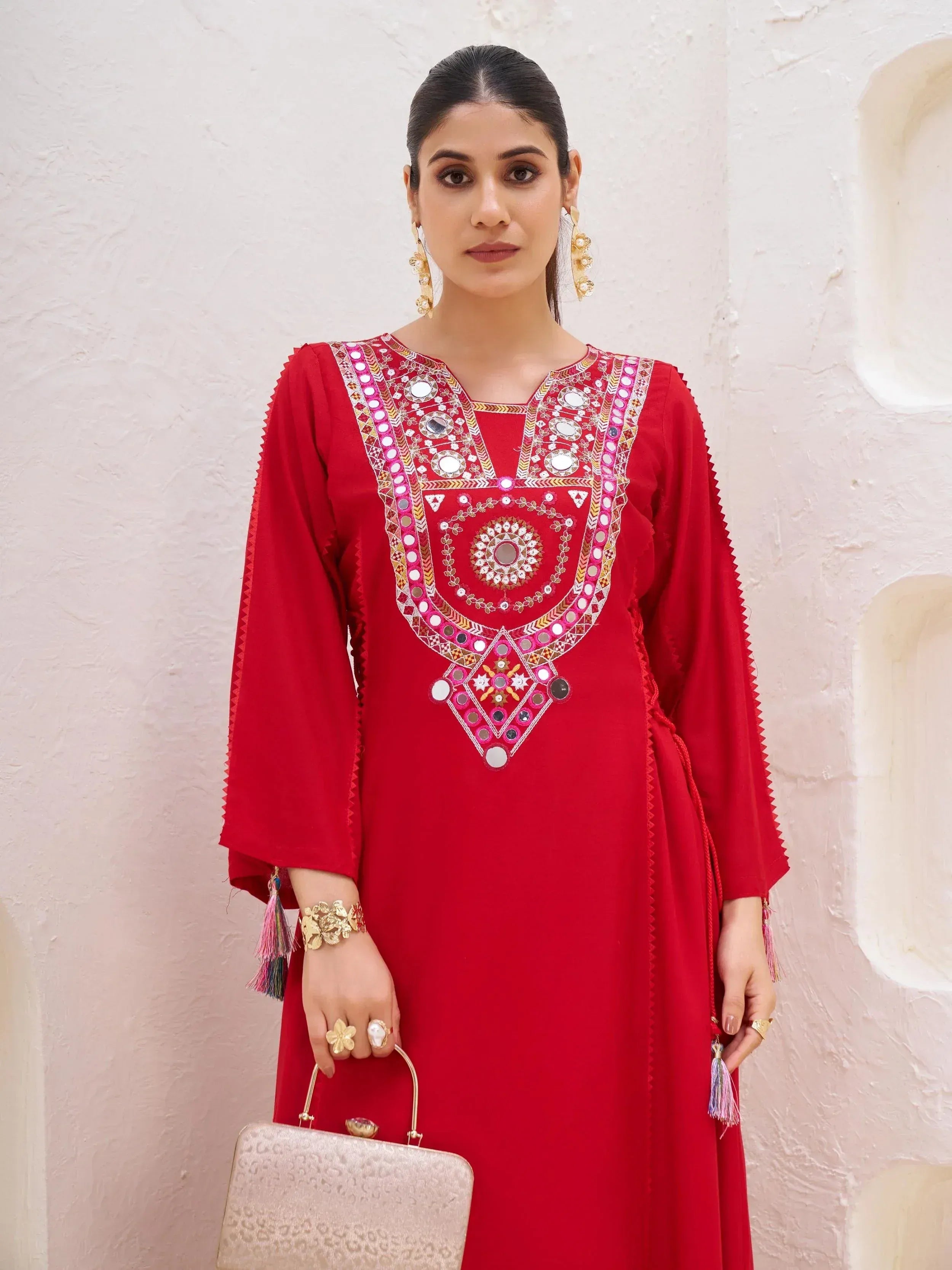Red ethnic kurti with mirror work and tassels, paired with gold jewelry and clutch