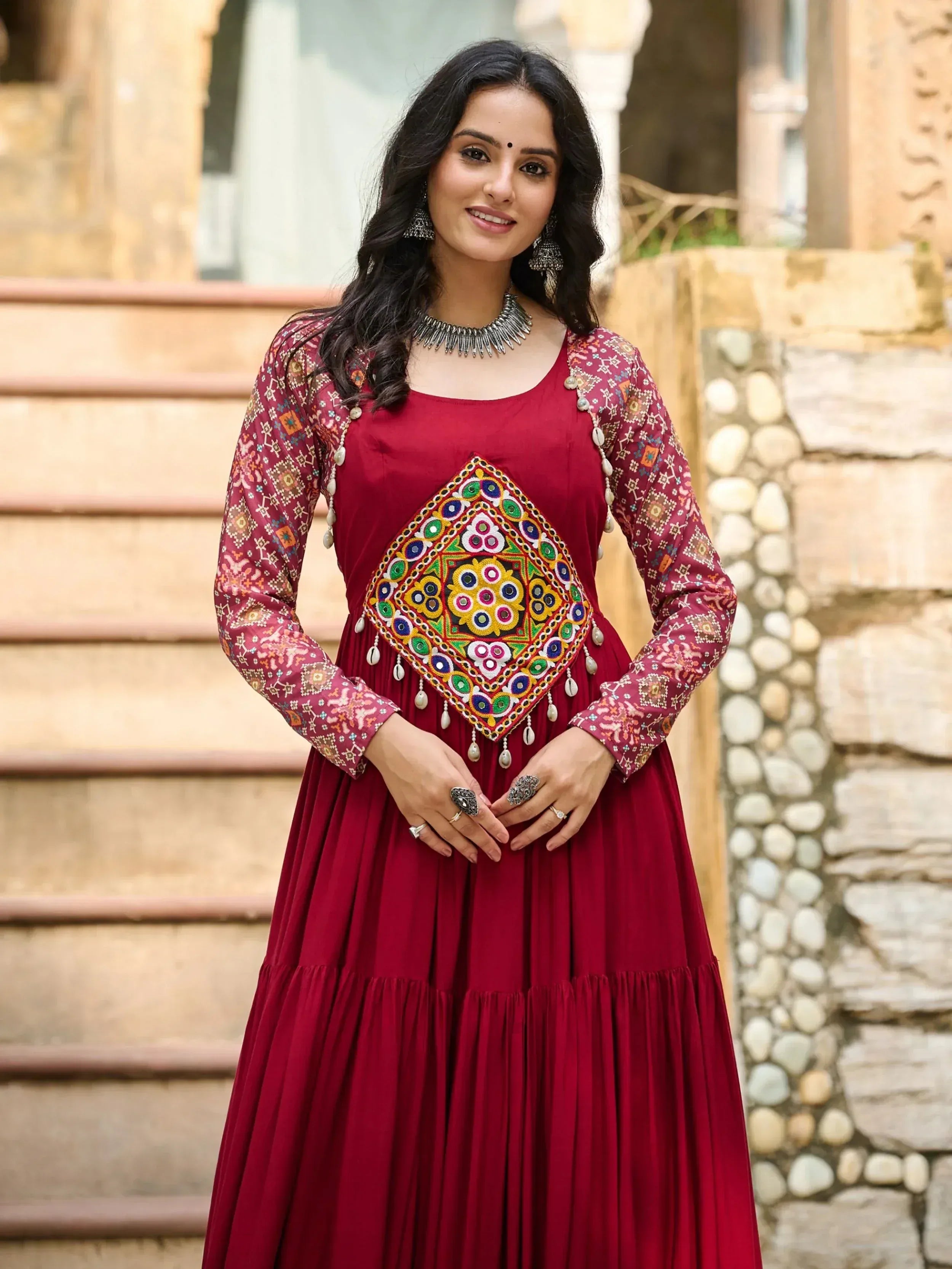 Maroon ethnic gown with colorful mirror work and printed sleeves, perfect for Indian festive occasions.