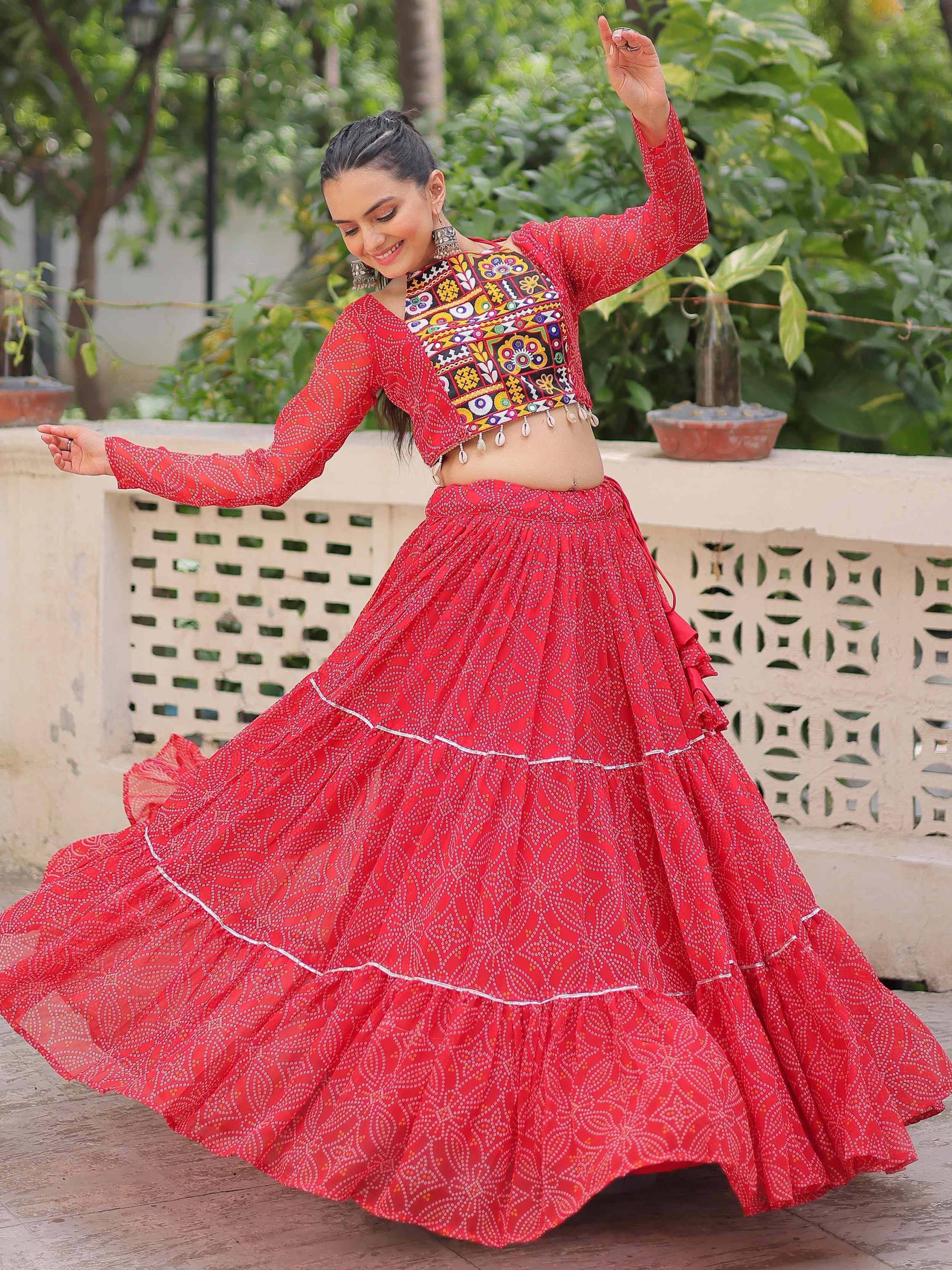 Woman dancing in vibrant red ethnic lehenga with mirror work blouse and flared skirt, perfect for festive occasions.