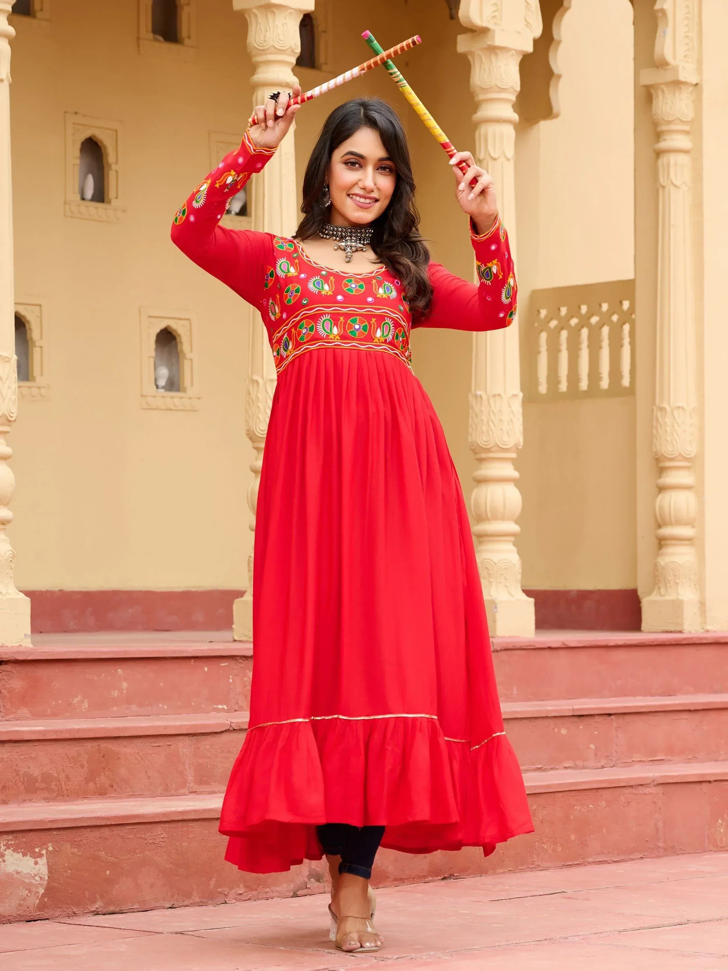 Woman in red embroidered ethnic gown with dandiya sticks, traditional Indian wear