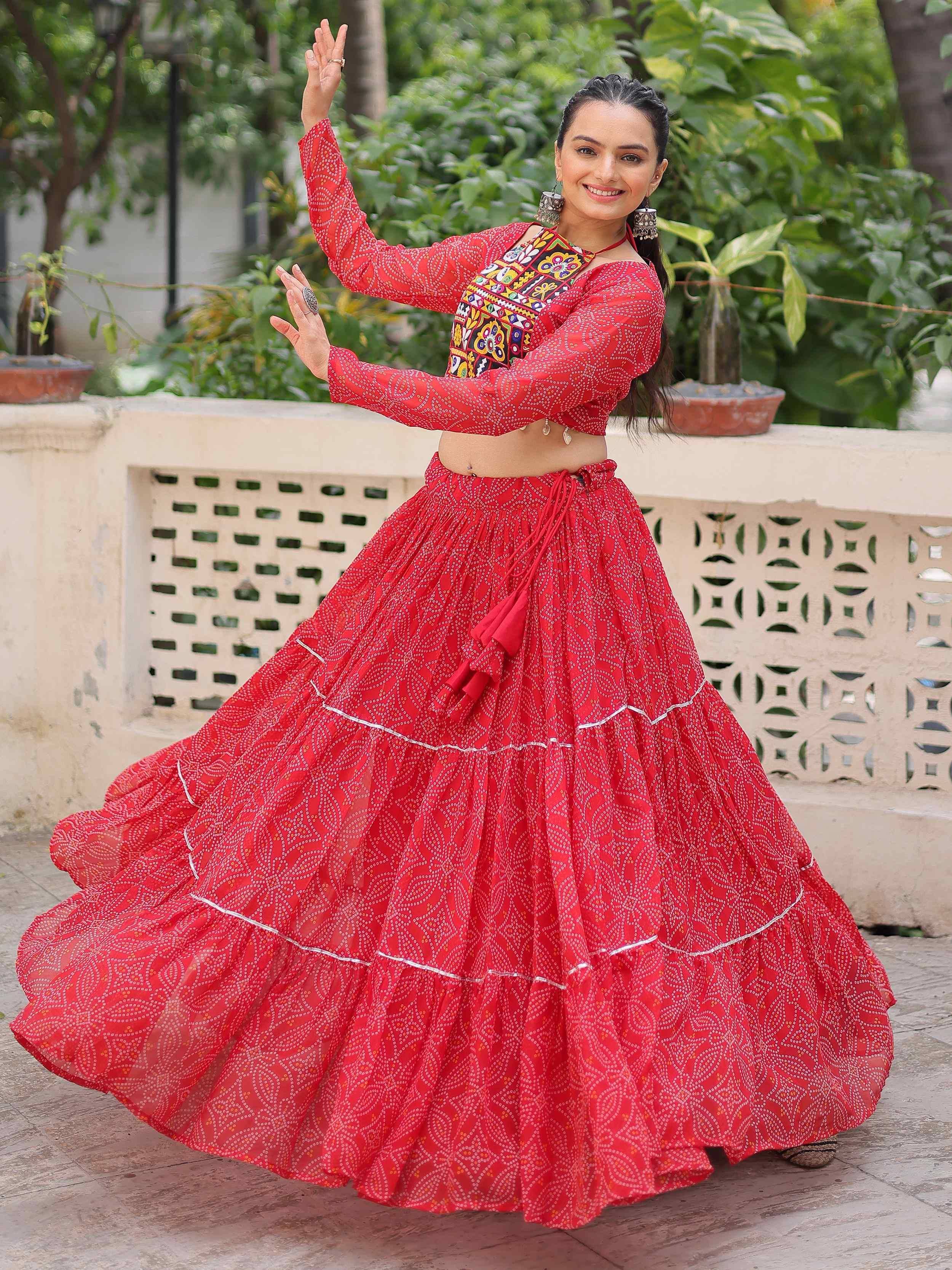 Woman in vibrant red ethnic lehenga choli with mirror work, dancing outdoors