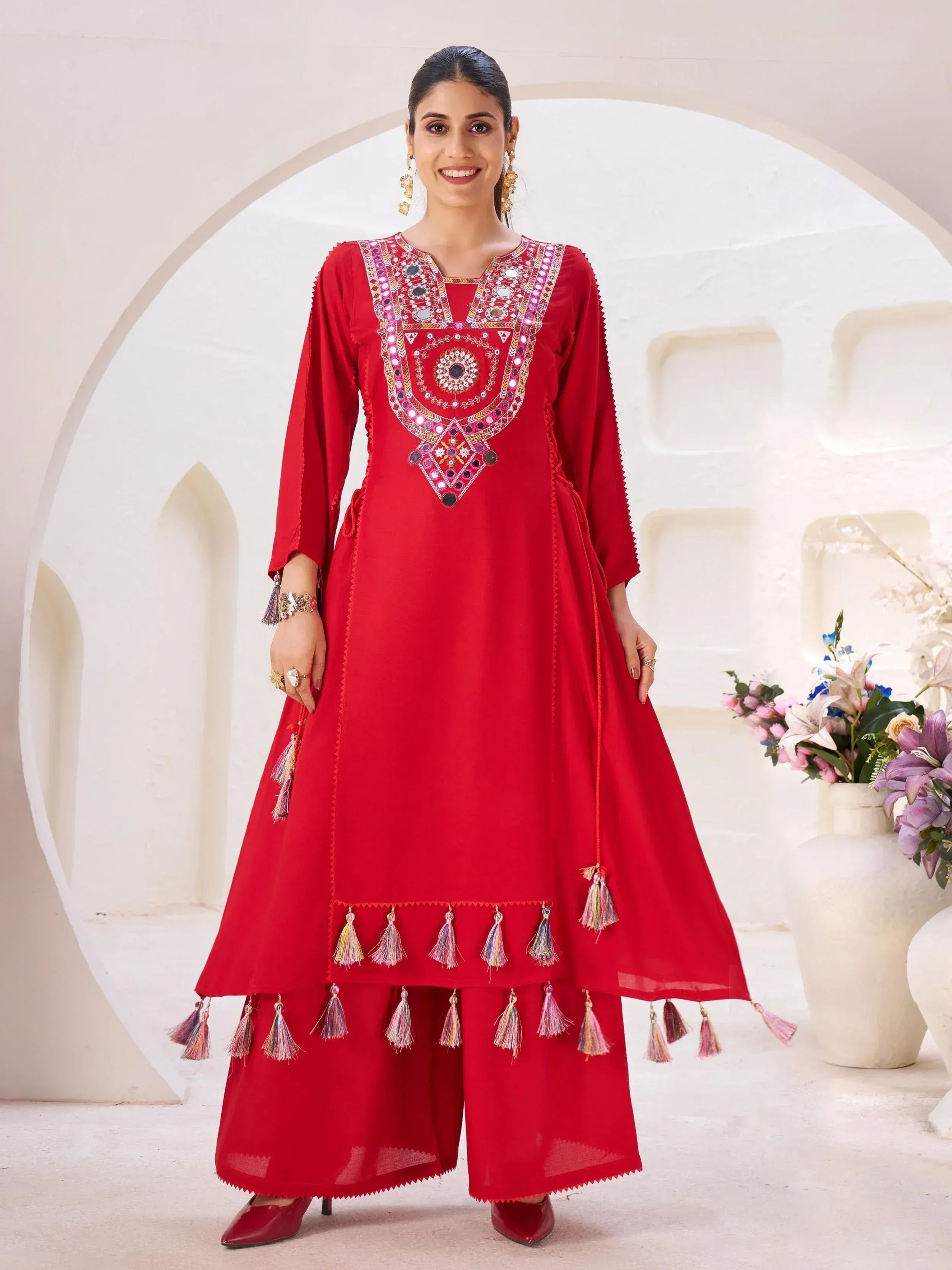Red ethnic anarkali suit with mirror work and tassels, perfect for Indian festive occasions
