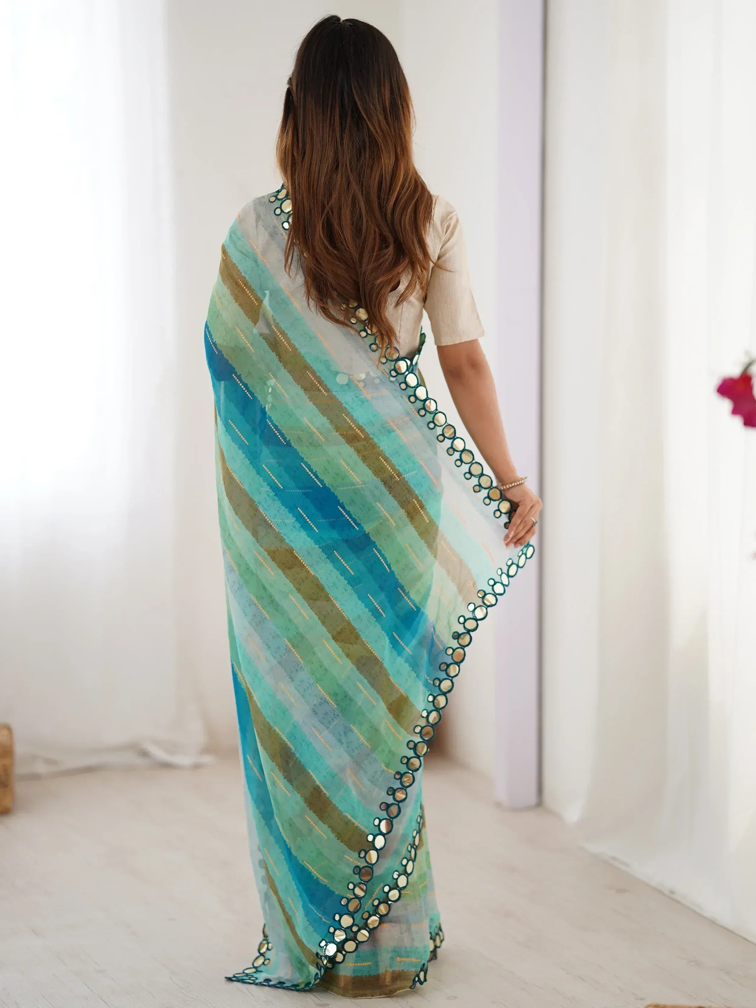 Woman wearing a blue-green striped saree with mirror work border, styled with a beige blouse for ethnic wear.