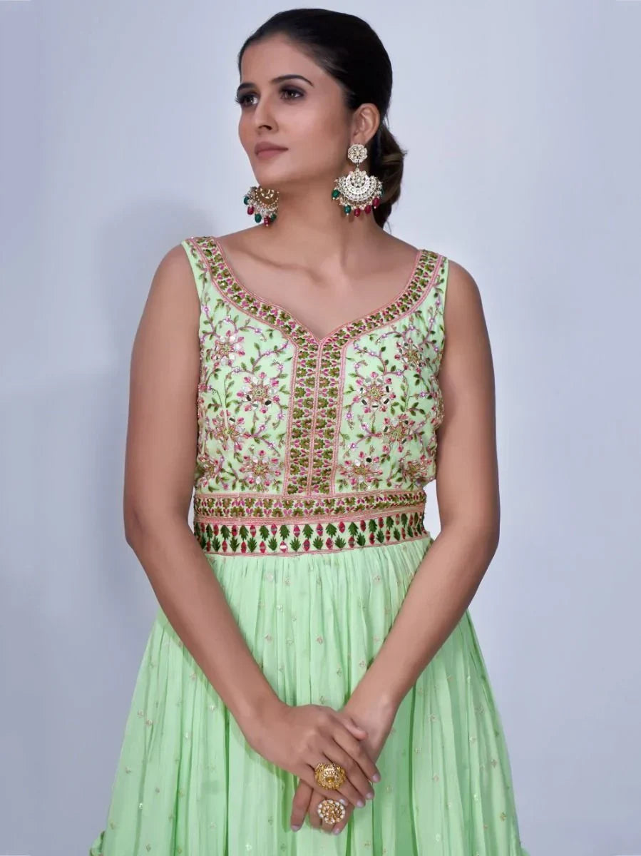 Woman in sleeveless light green embroidered gown with floral patterns and statement earrings