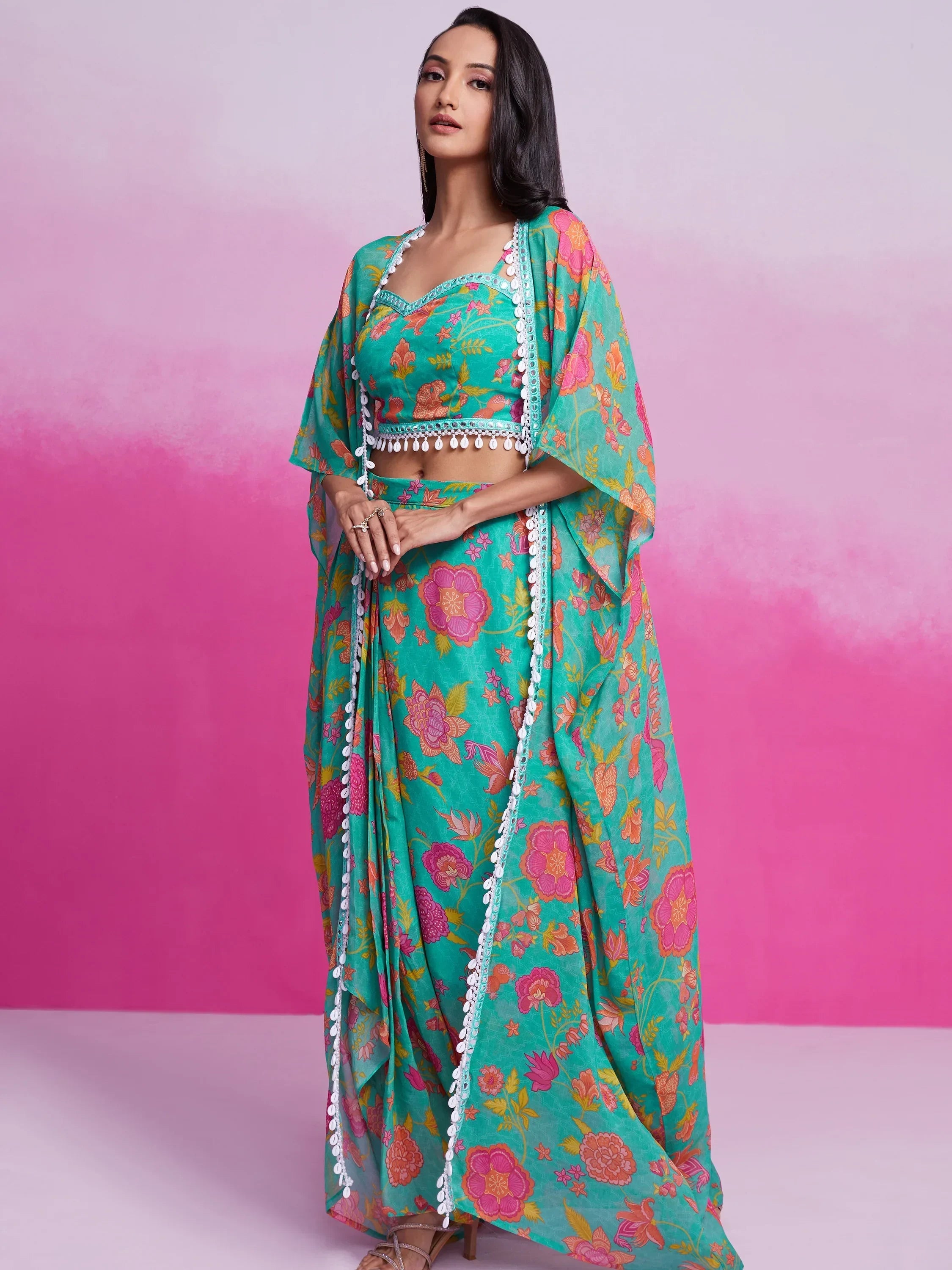 Woman in teal floral printed saree with white lace border standing against pink background