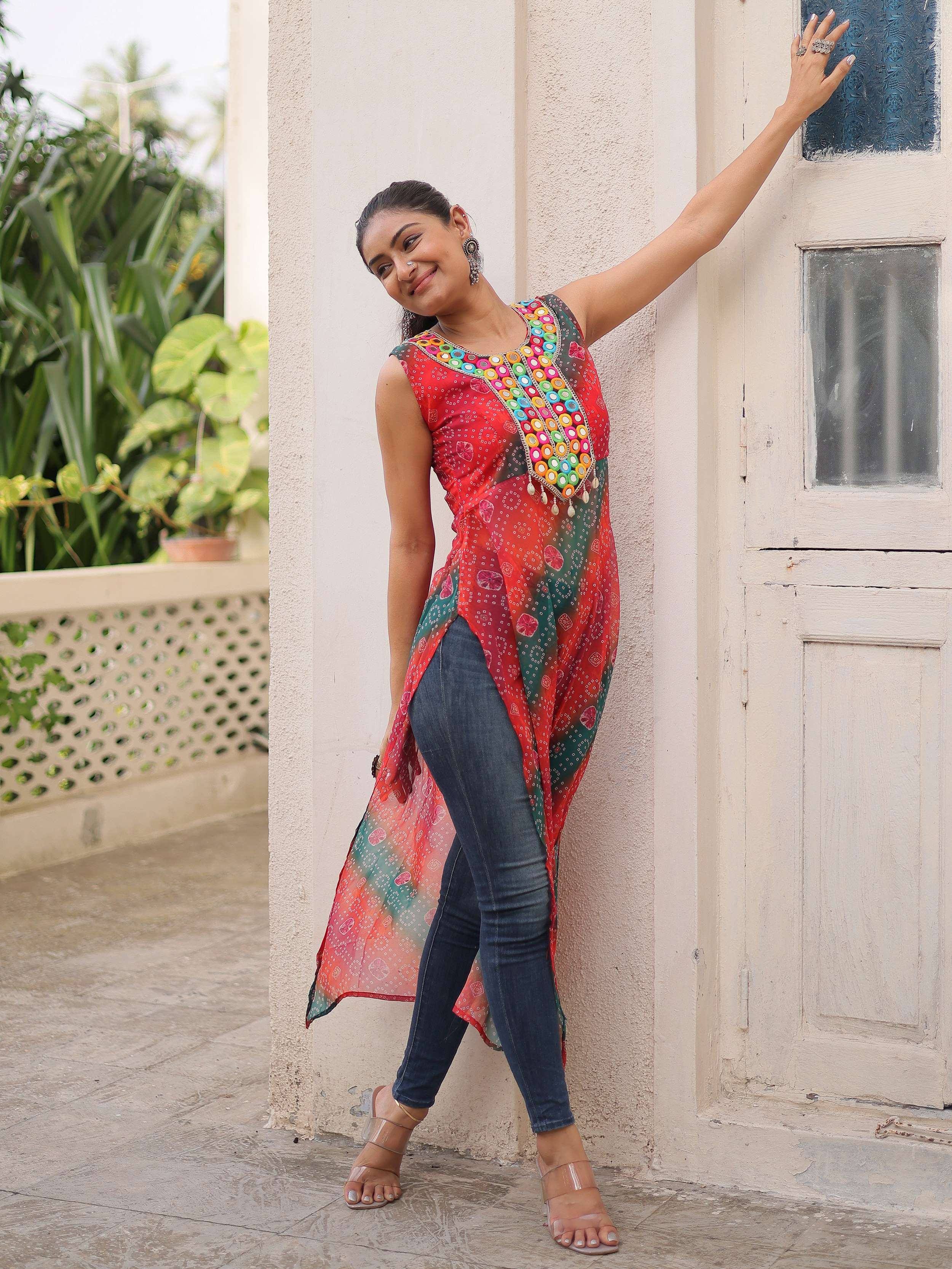 Woman in colorful embroidered ethnic kurti with mirror work, paired with jeans, standing by a door