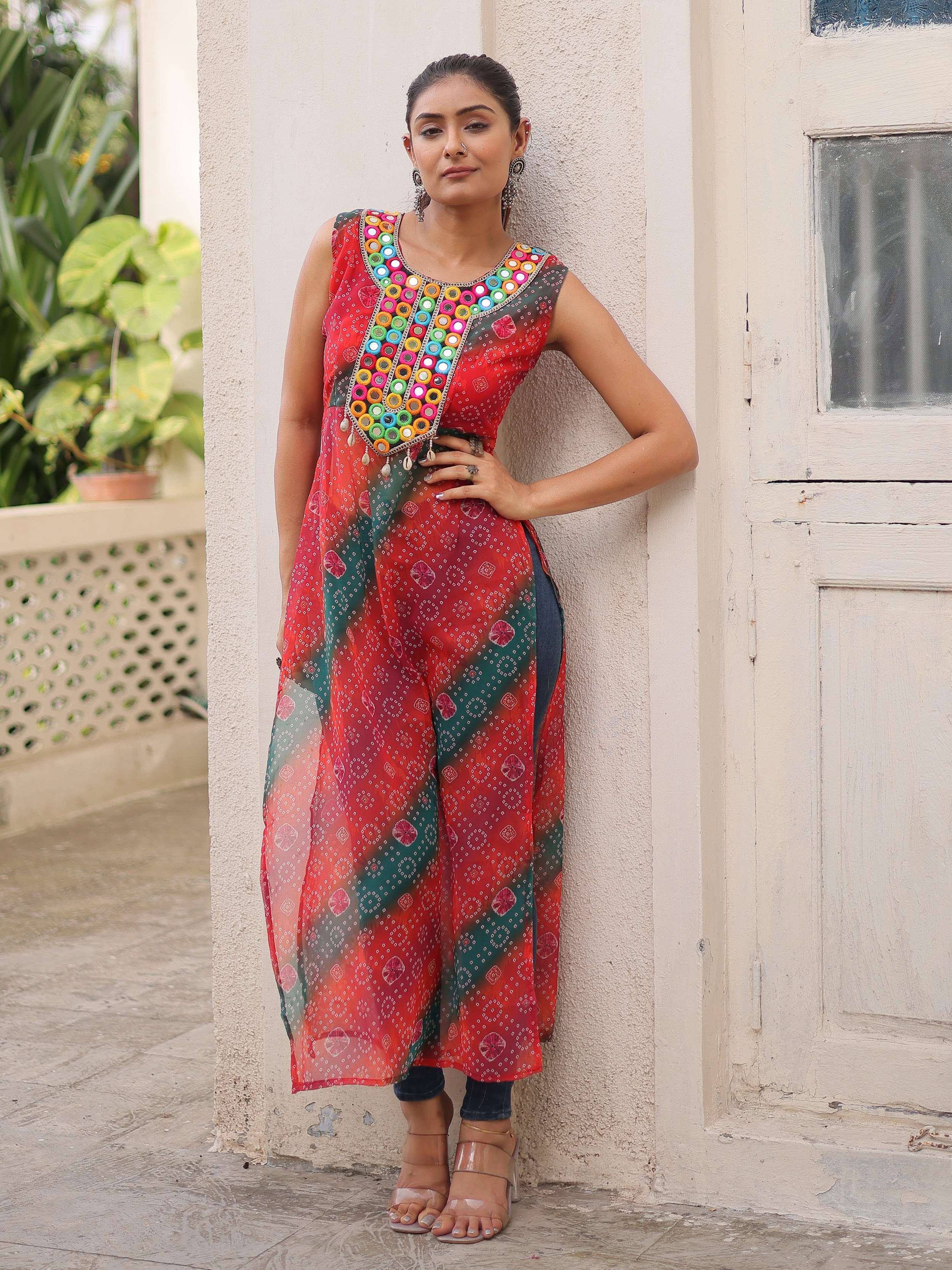 Woman in red and green printed ethnic kurta with mirror work, paired with jeans, standing outdoors