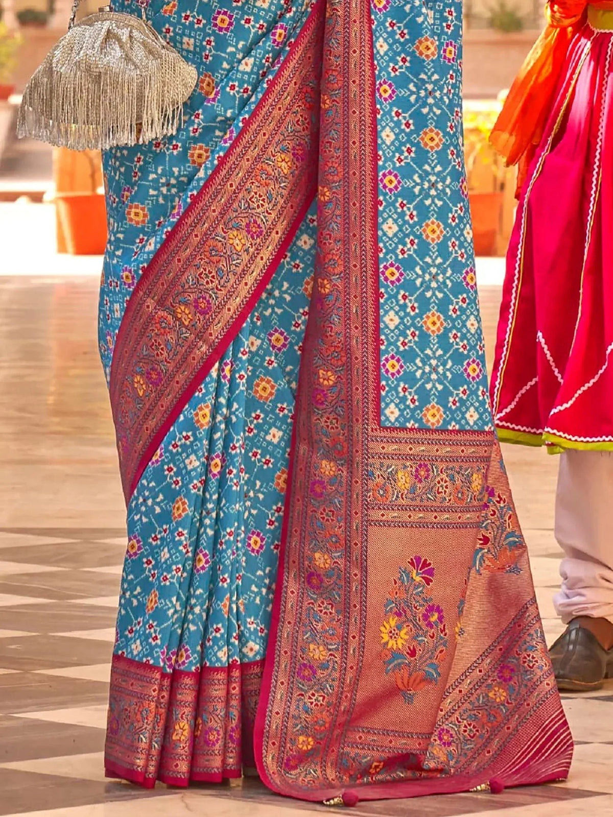Blue floral print saree with red border, ethnic Indian wear, paired with silver fringed clutch