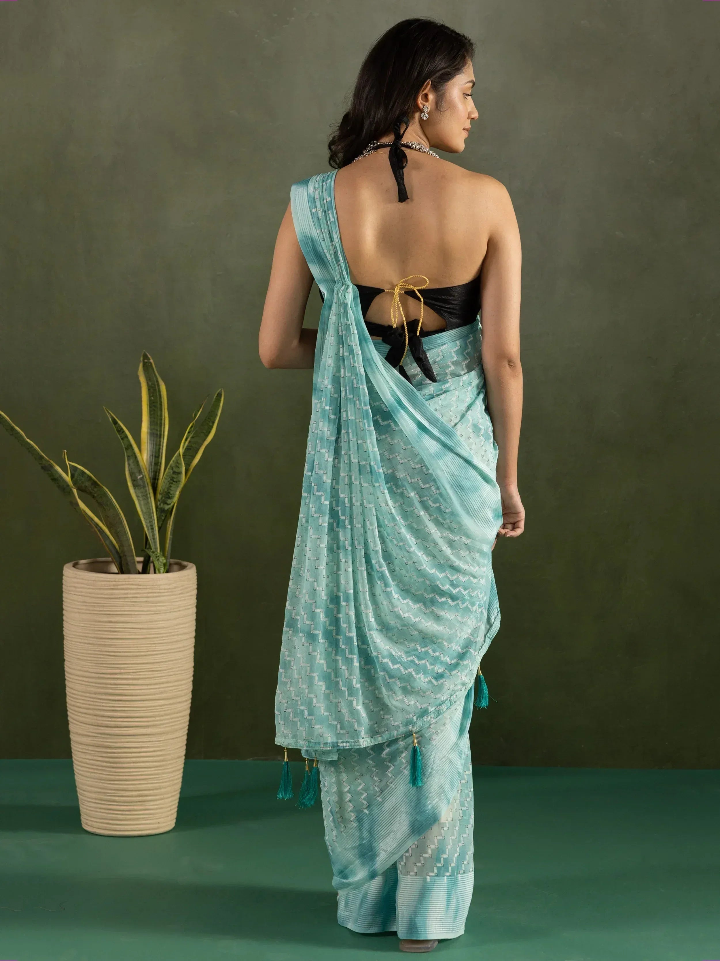 Woman in backless teal saree with geometric print and tassels, styled with black blouse and ethnic jewelry