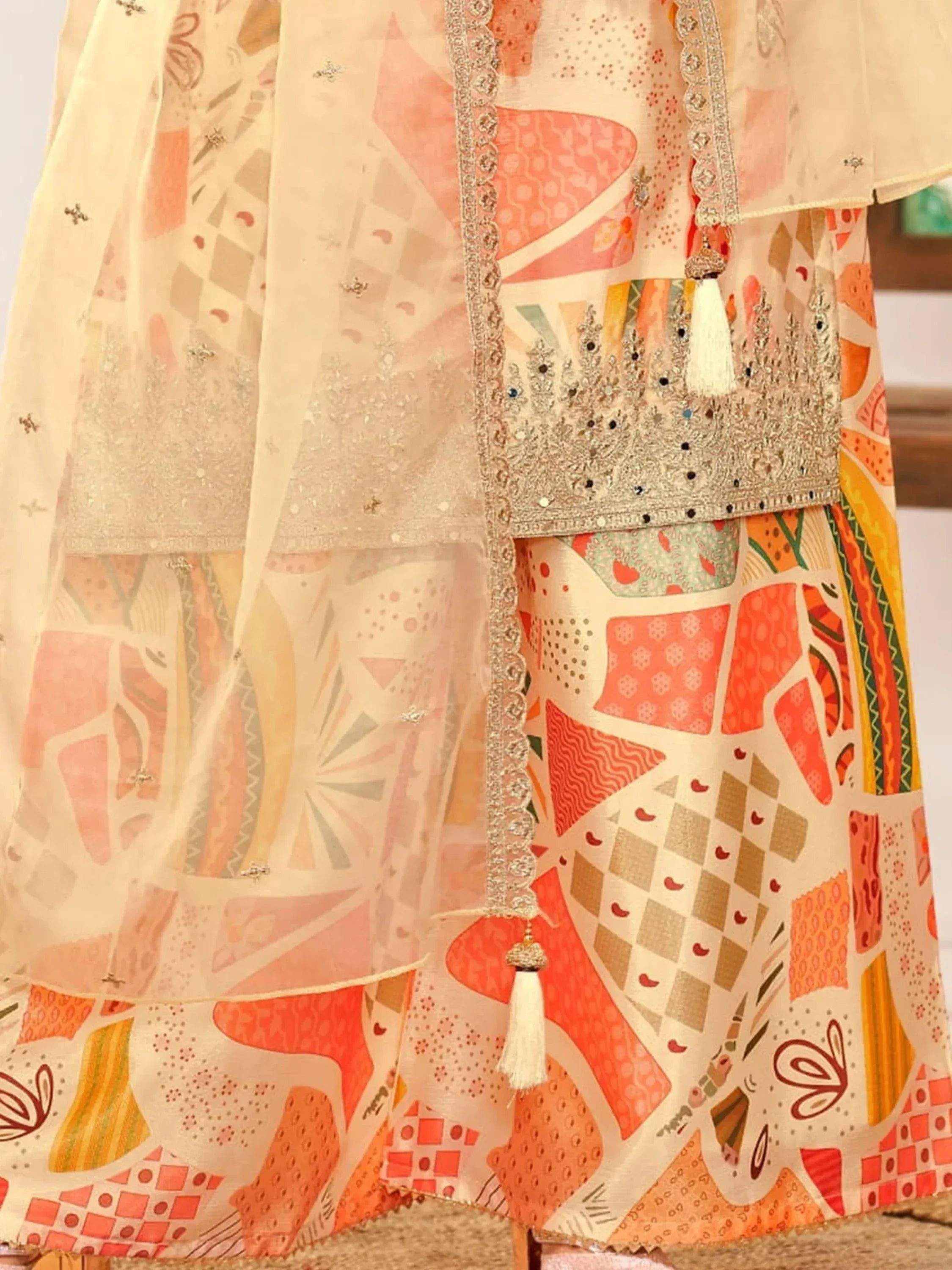 Ethnic printed lehenga choli with embroidered dupatta and tassels, vibrant geometric patterns in peach, orange, and gold tones