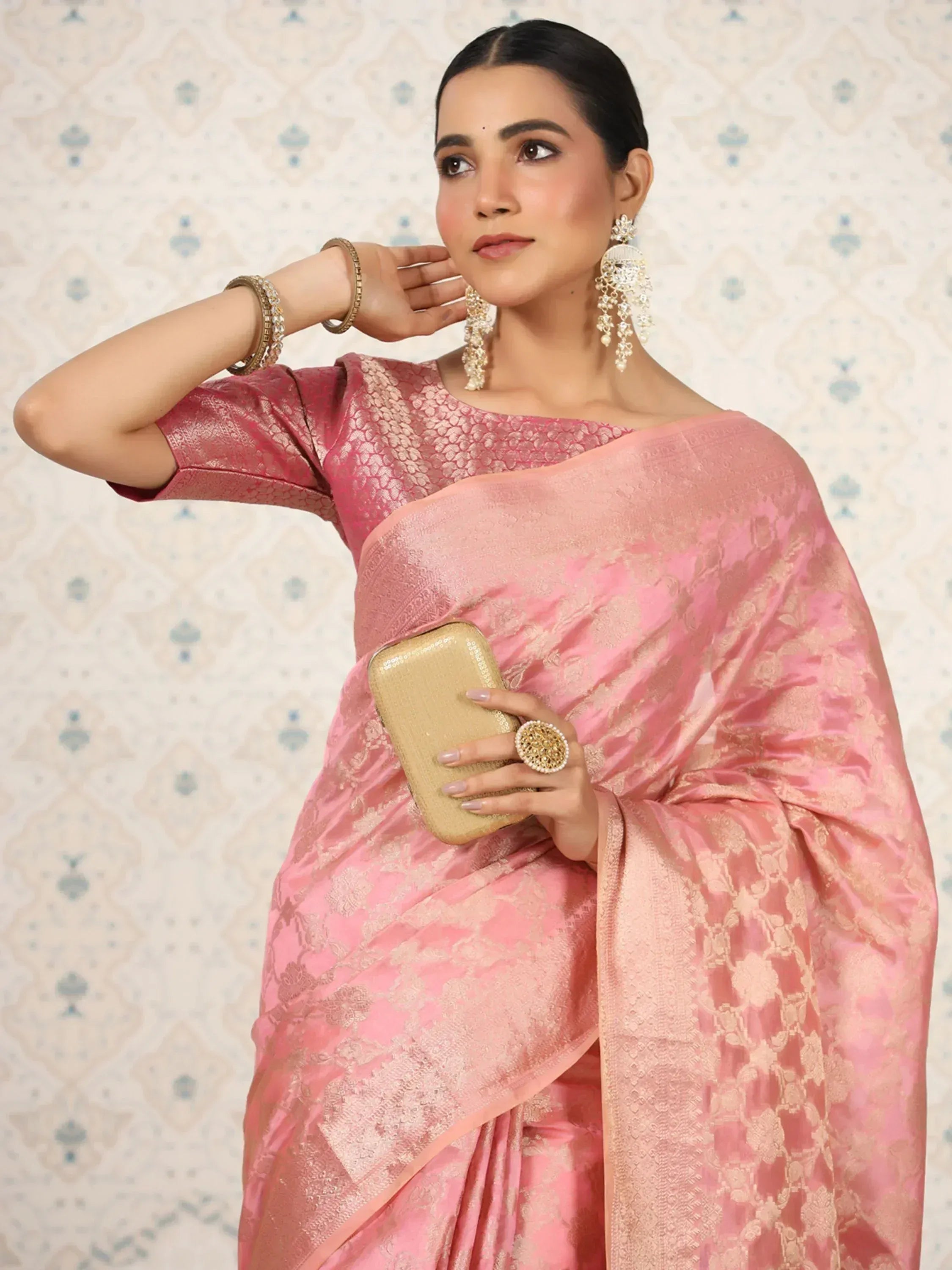 Pink designer saree with gold embroidery, paired with statement jewelry and clutch, perfect for ethnic occasions