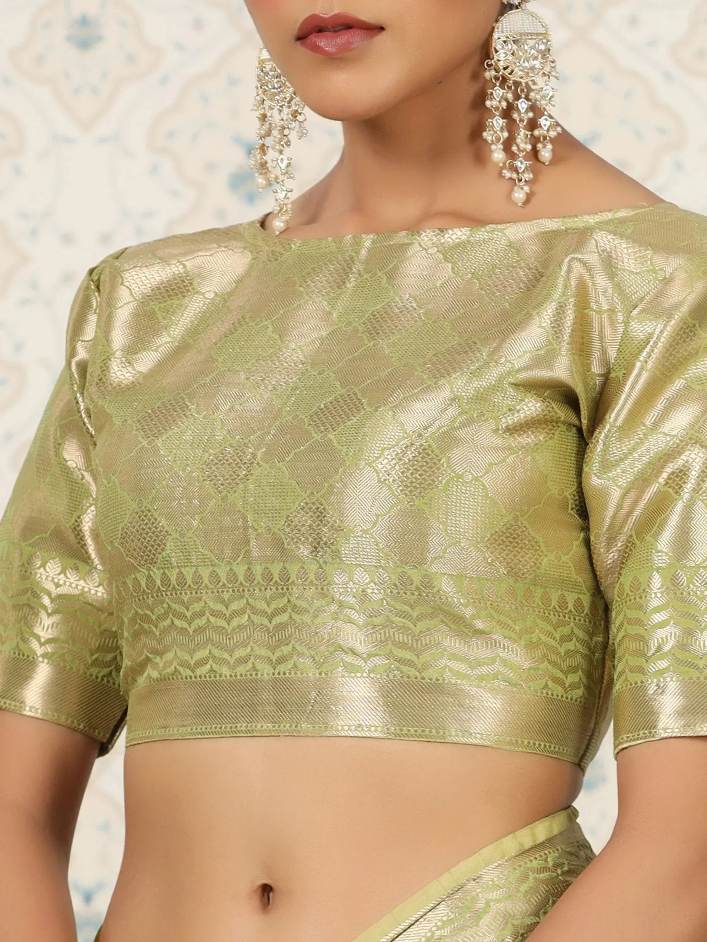 Elegant green and gold brocade crop top with intricate patterns, paired with matching saree and statement earrings.
