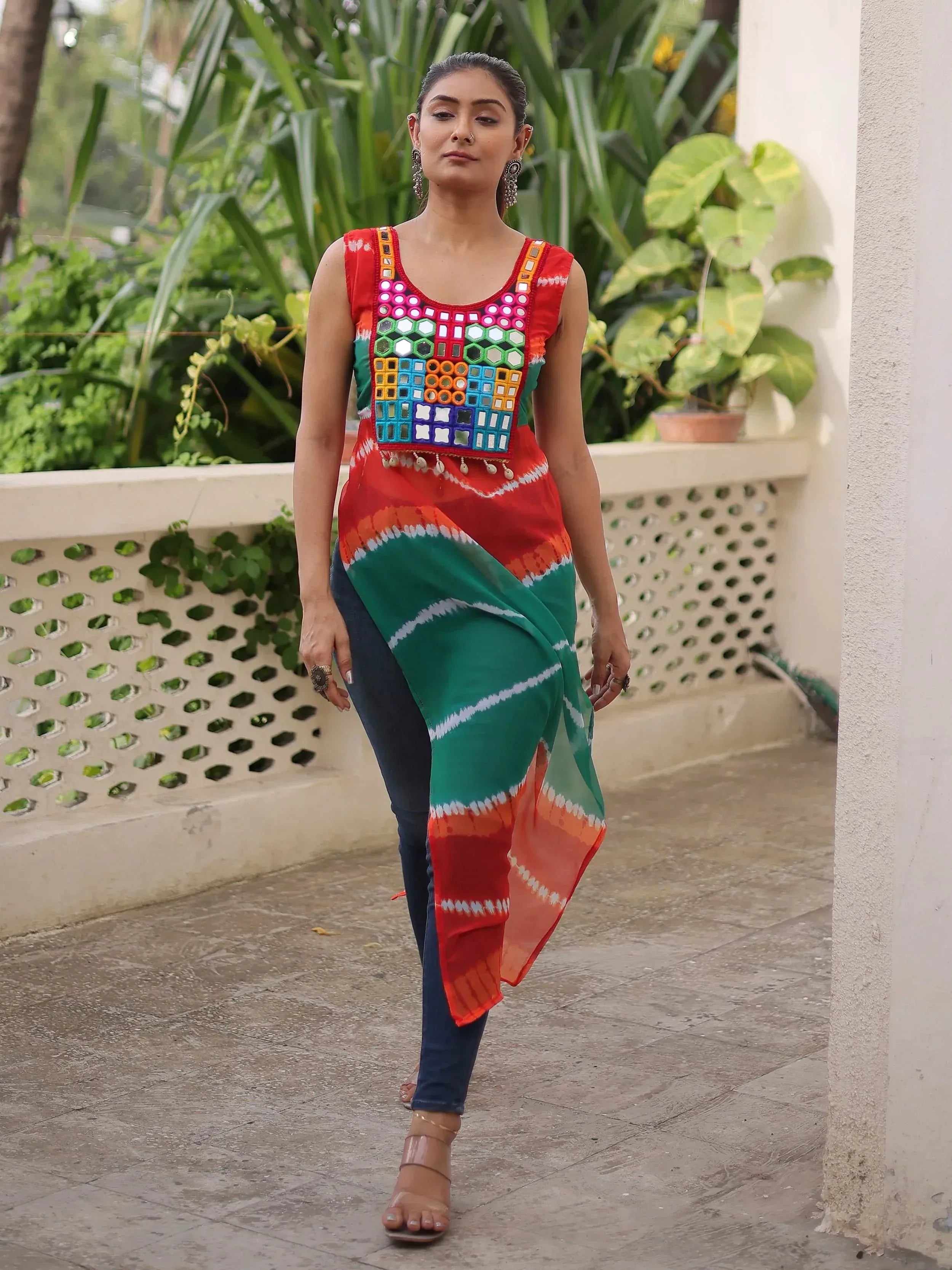 Woman wearing colorful mirror-work ethnic top with tie-dye print and jeans, styled for Indian fashion.