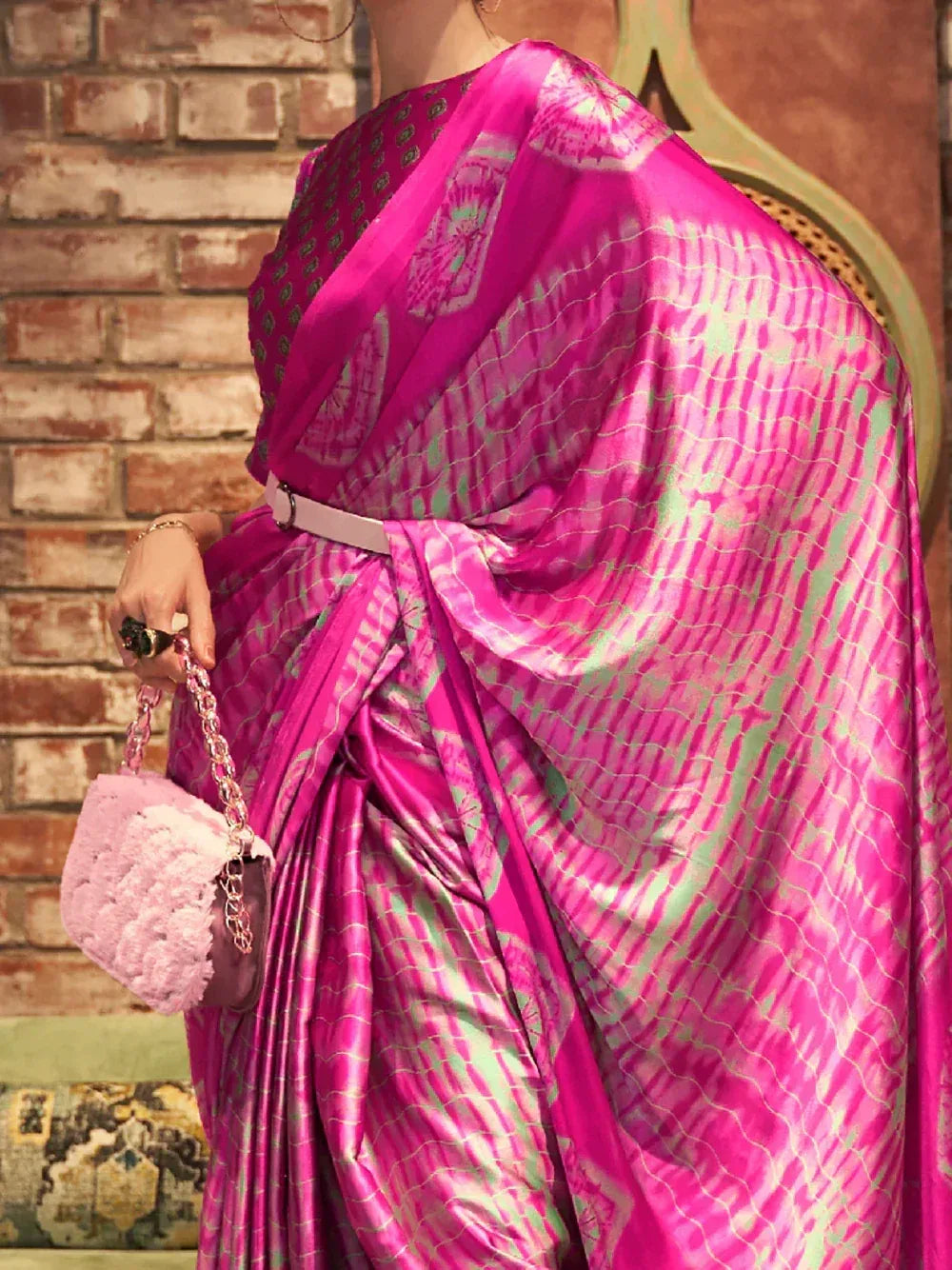 Vibrant pink ikat saree with green patterns, styled with belt and pink handbag, perfect for ethnic occasions.