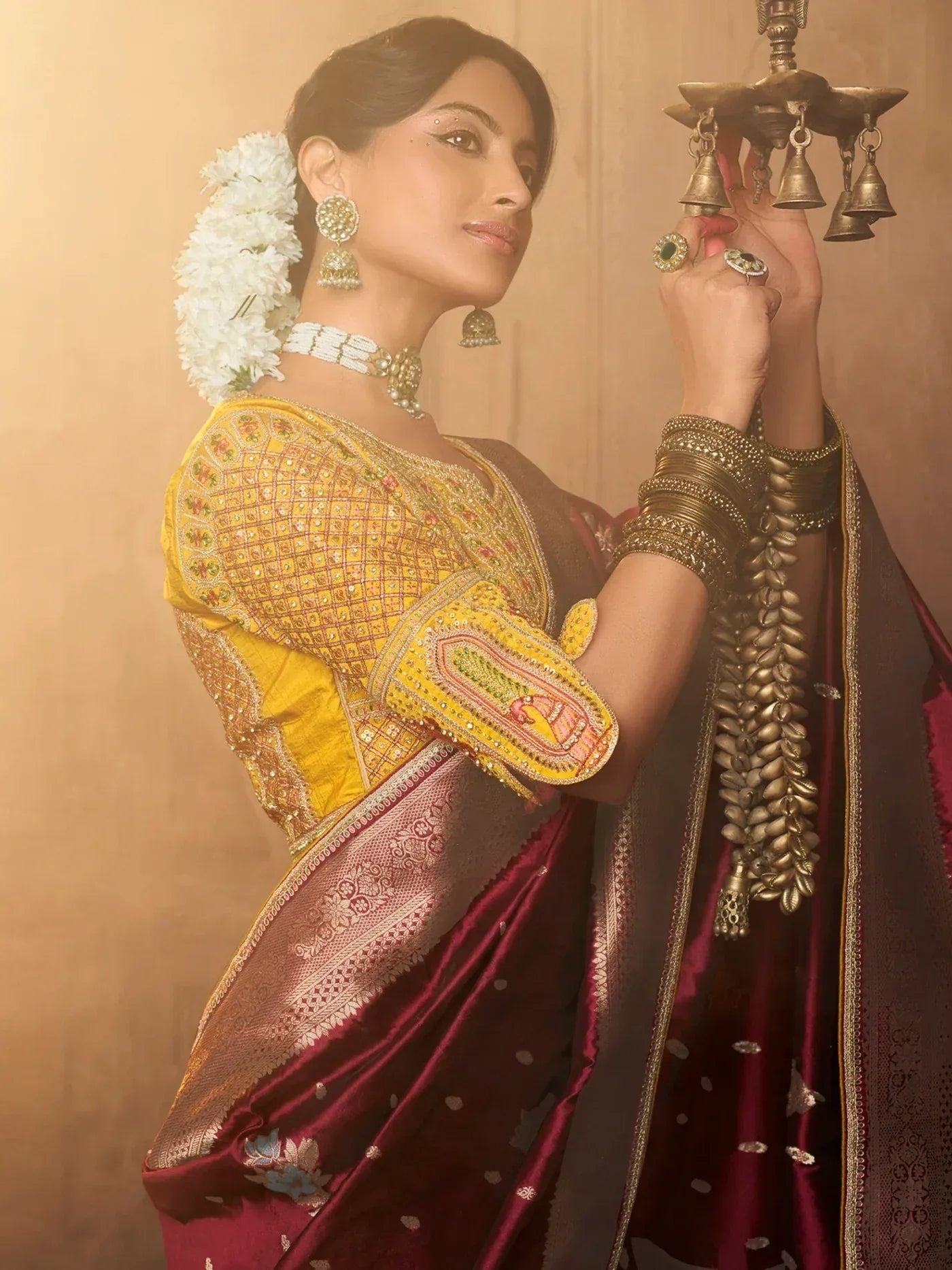 Woman in maroon silk saree with yellow embroidered blouse, floral hair accessory, and temple bells