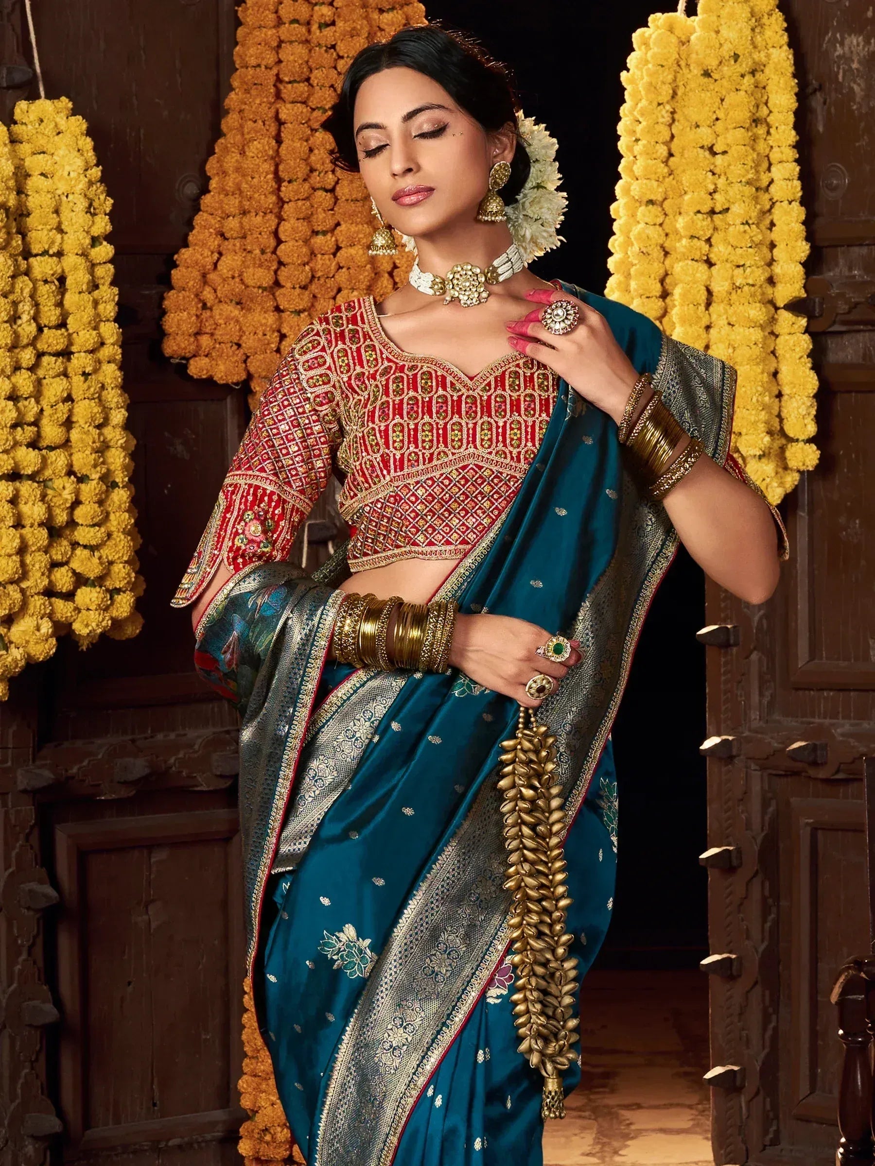Teal saree with red embroidered blouse, gold jewelry, and floral garlands for Indian ethnic wear