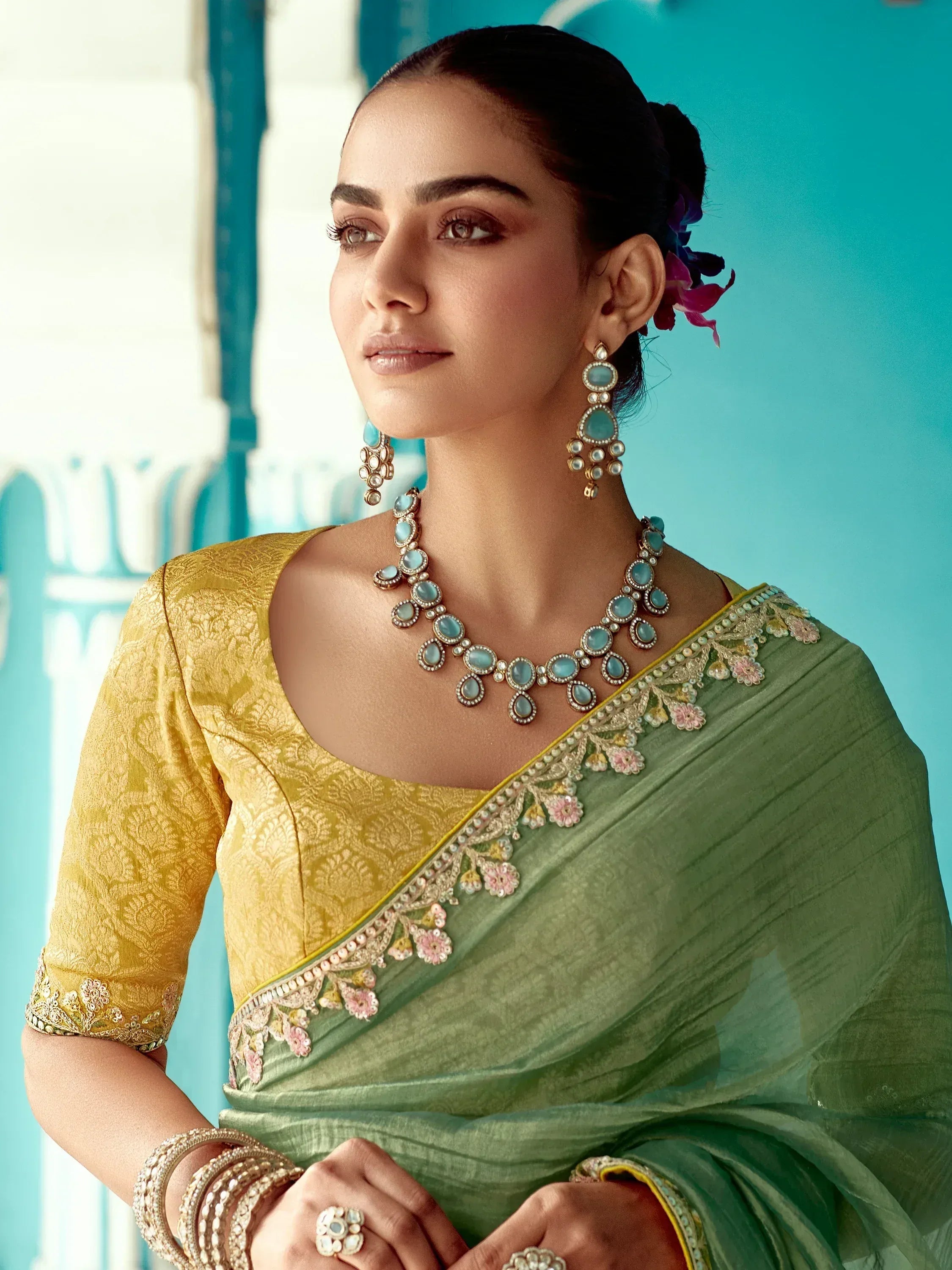 Elegant woman in green saree with gold blouse, floral embroidery, and turquoise jewelry, showcasing Indian ethnic wear.