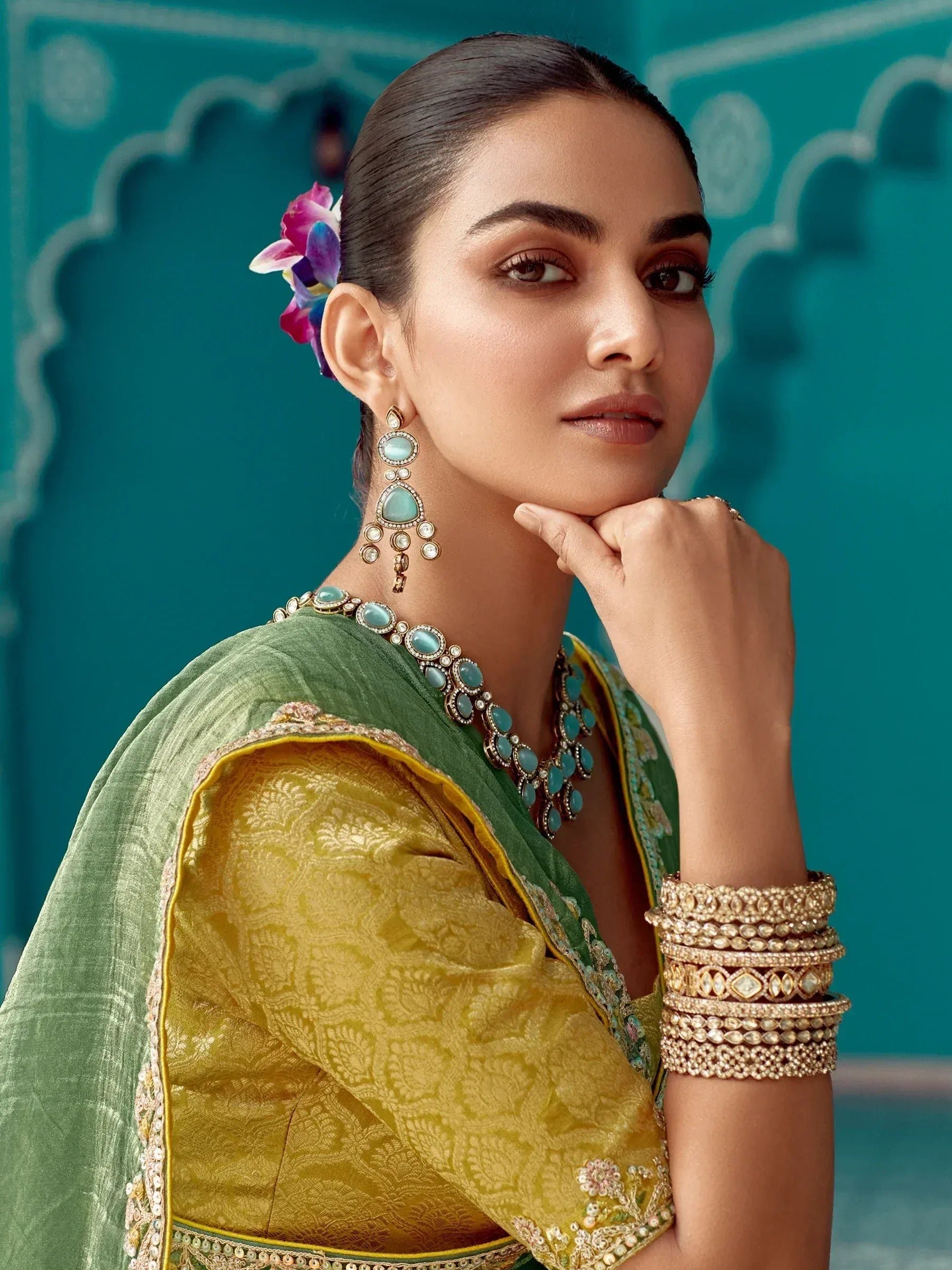 Woman in green and gold ethnic saree with turquoise jewelry and floral hair accessory