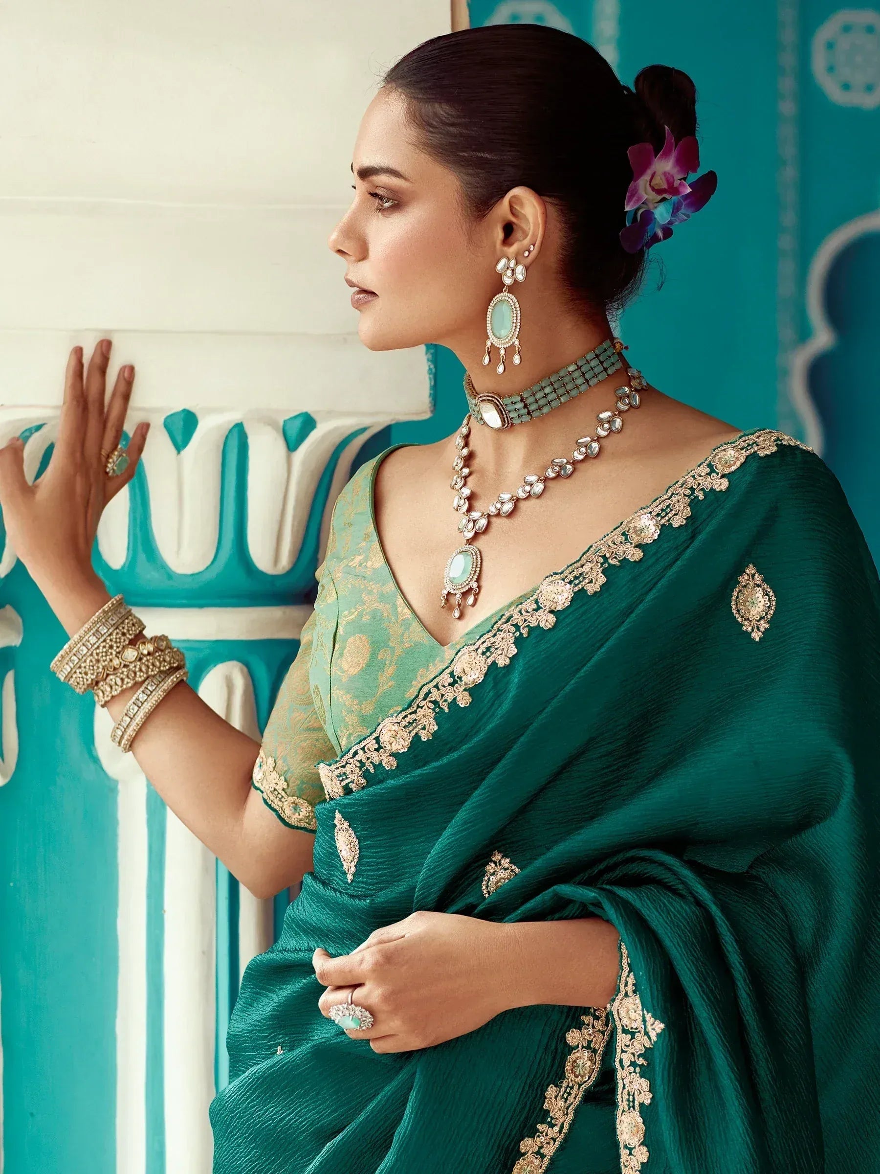 Elegant woman in emerald green designer saree with gold embroidery, paired with traditional jewelry and floral hair accessory.
