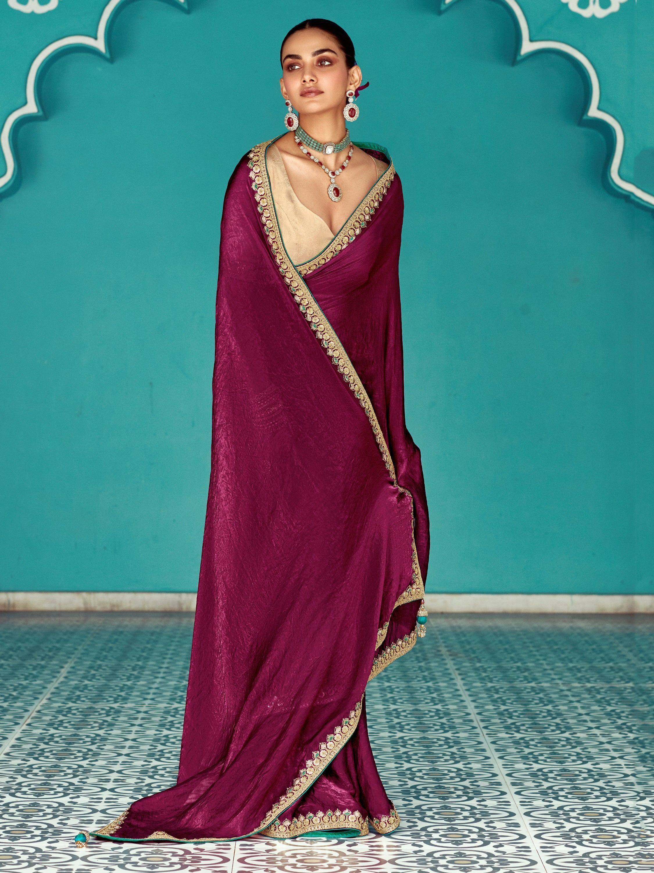 Elegant maroon saree with gold and green embroidery, styled with traditional jewelry against a teal backdrop.