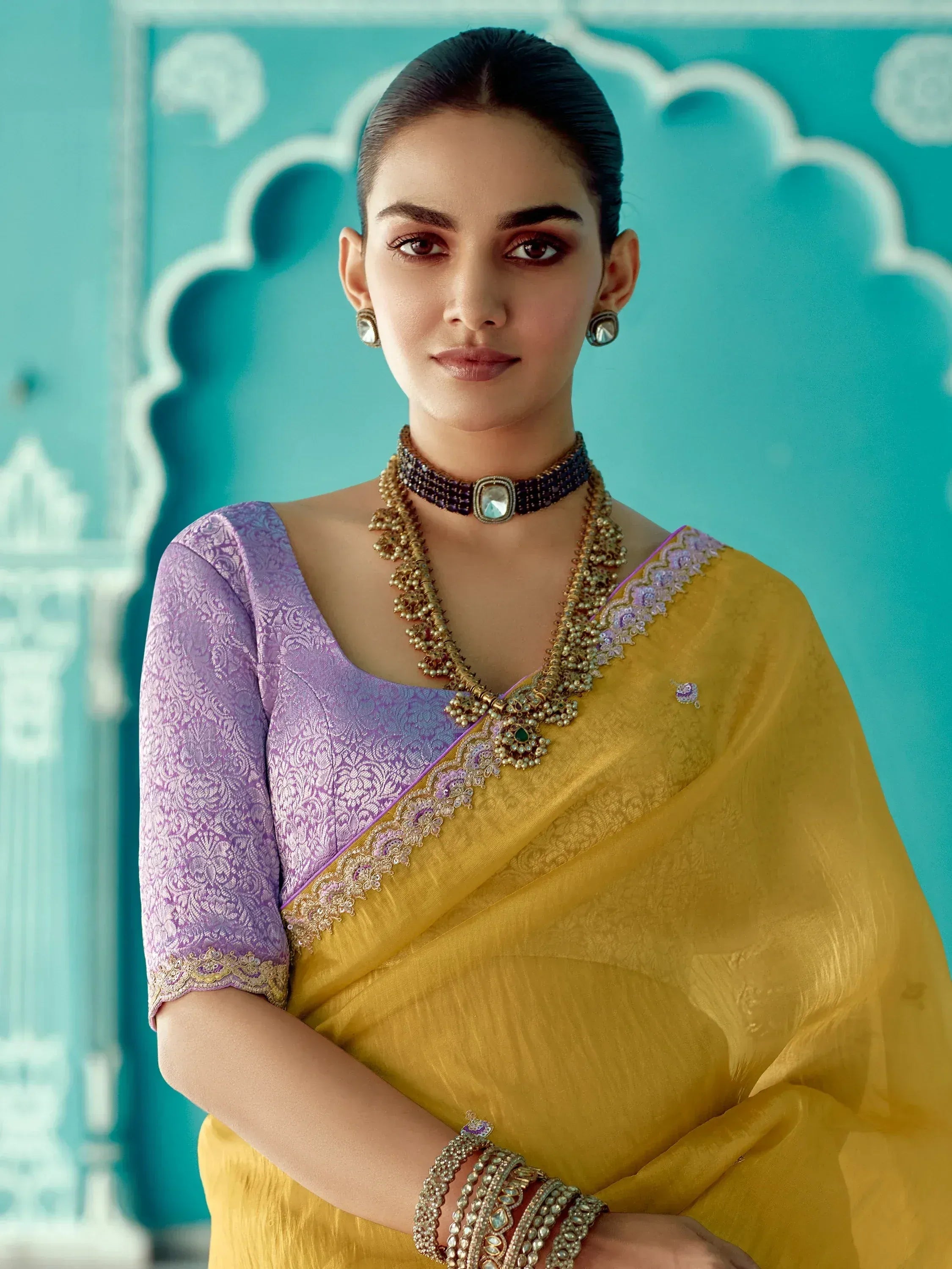 Woman in yellow saree with purple blouse, traditional Indian ethnic wear, ornate jewelry, teal backdrop