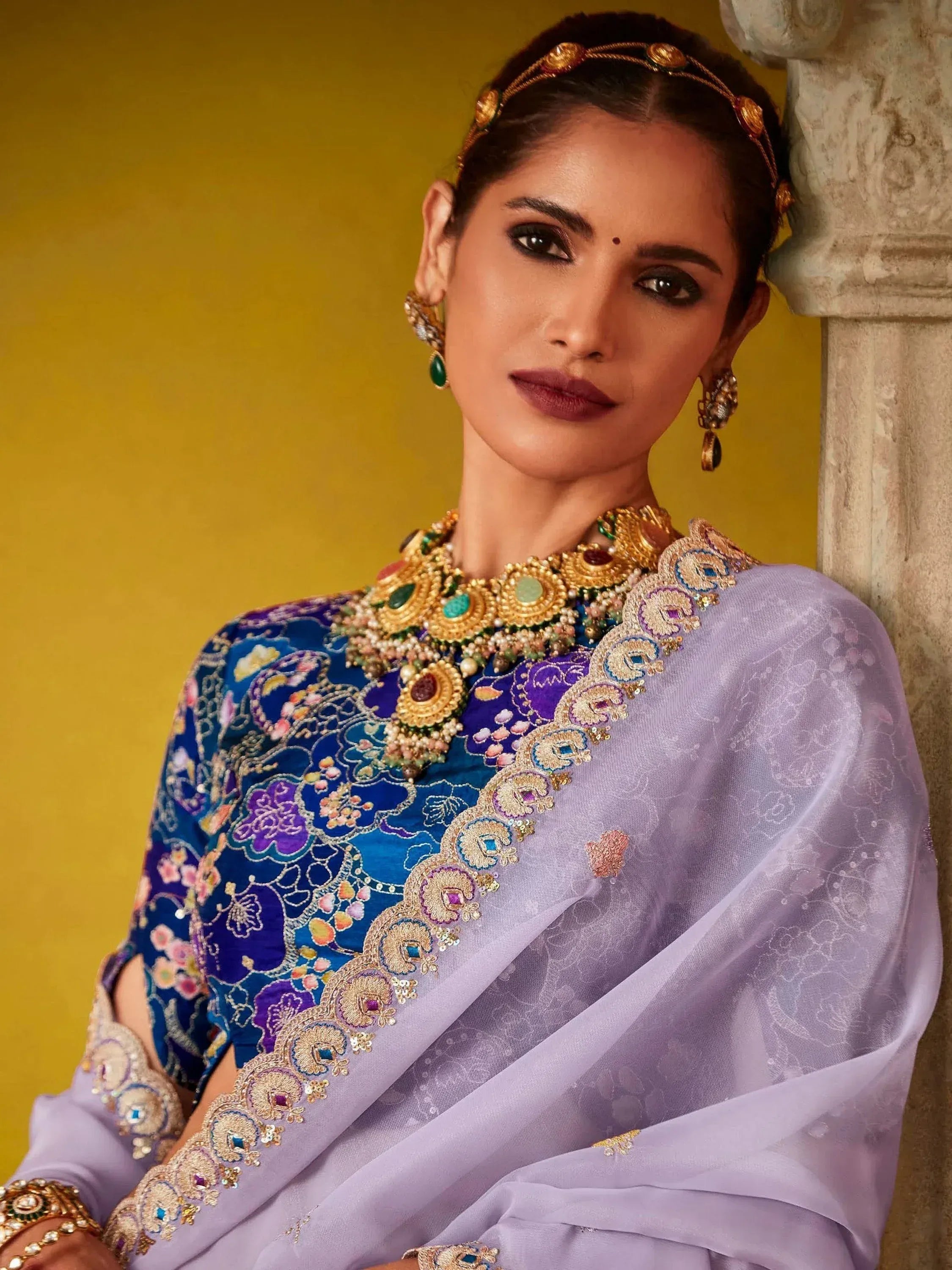 Woman in embroidered blue and purple Indian ethnic saree with gold jewelry, perfect for weddings or festive occasions.