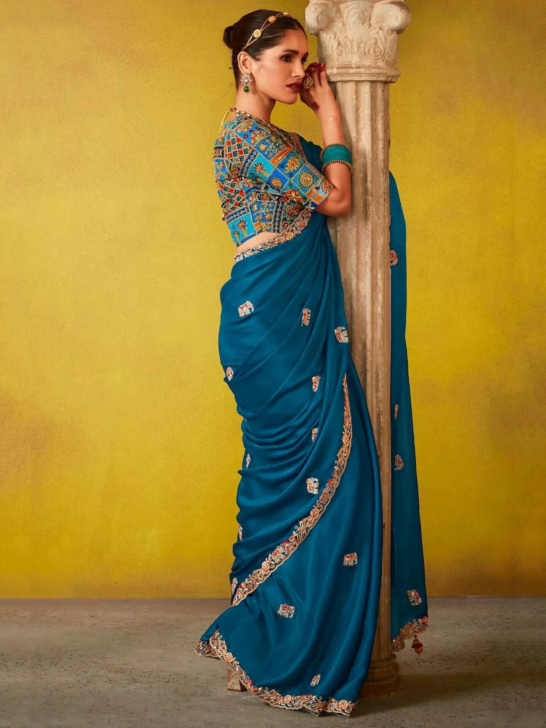 Woman in blue embroidered saree with elephant motifs, traditional Indian ethnic wear, standing by pillar